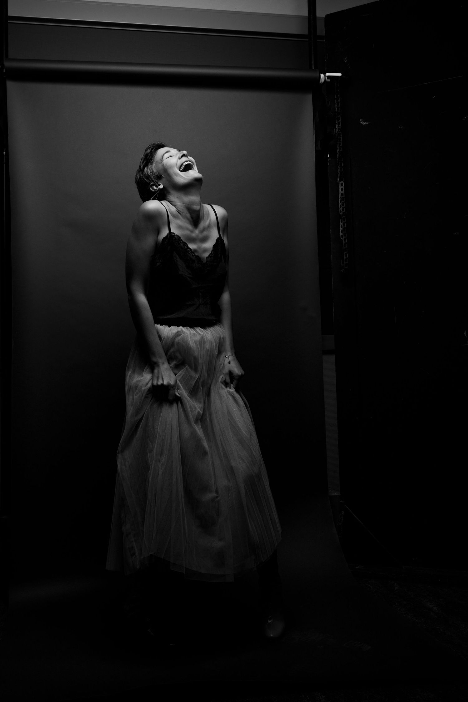 Woman in black top and white tulle skirt laughing with head thrown back in black and white studio photo.