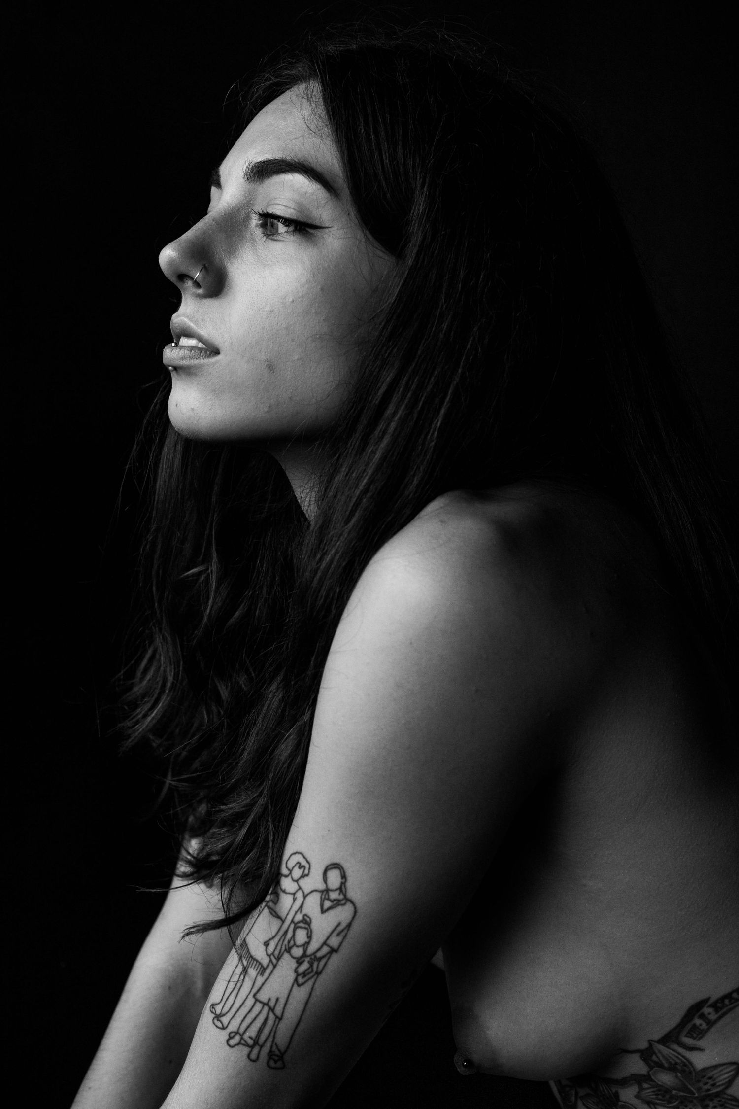 Black and white profile portrait of tattooed brunette woman against dark background.