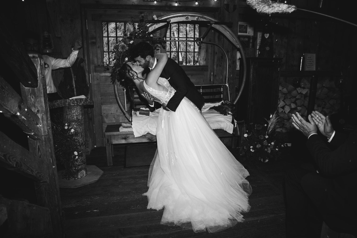 Bride and groom share first kiss in rustic barn venue in dramatic black and white photo.