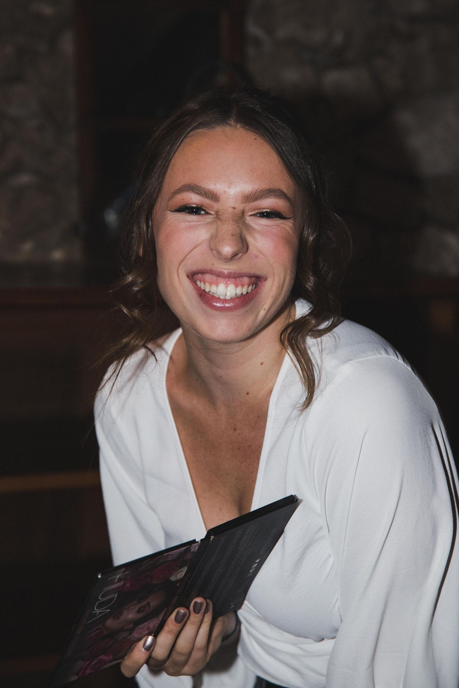 Happy young woman in white blouse smiling brightly while holding a makeup palette.