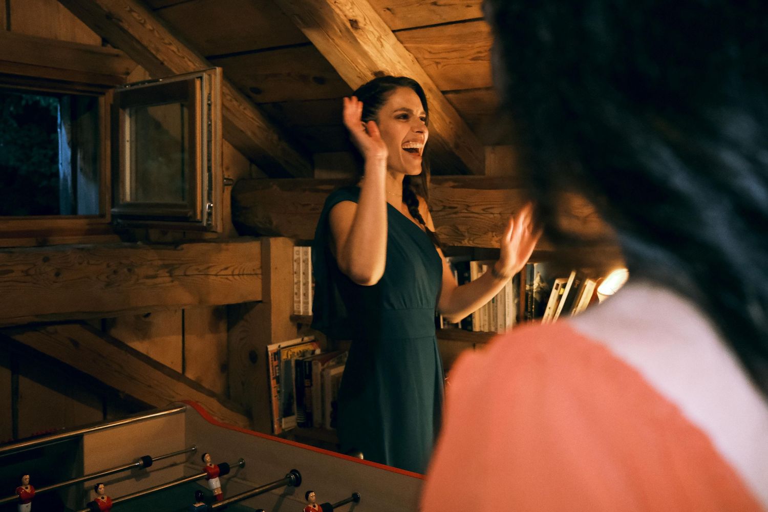 Woman in teal dress laughs expressively while chatting near foosball table in barn.