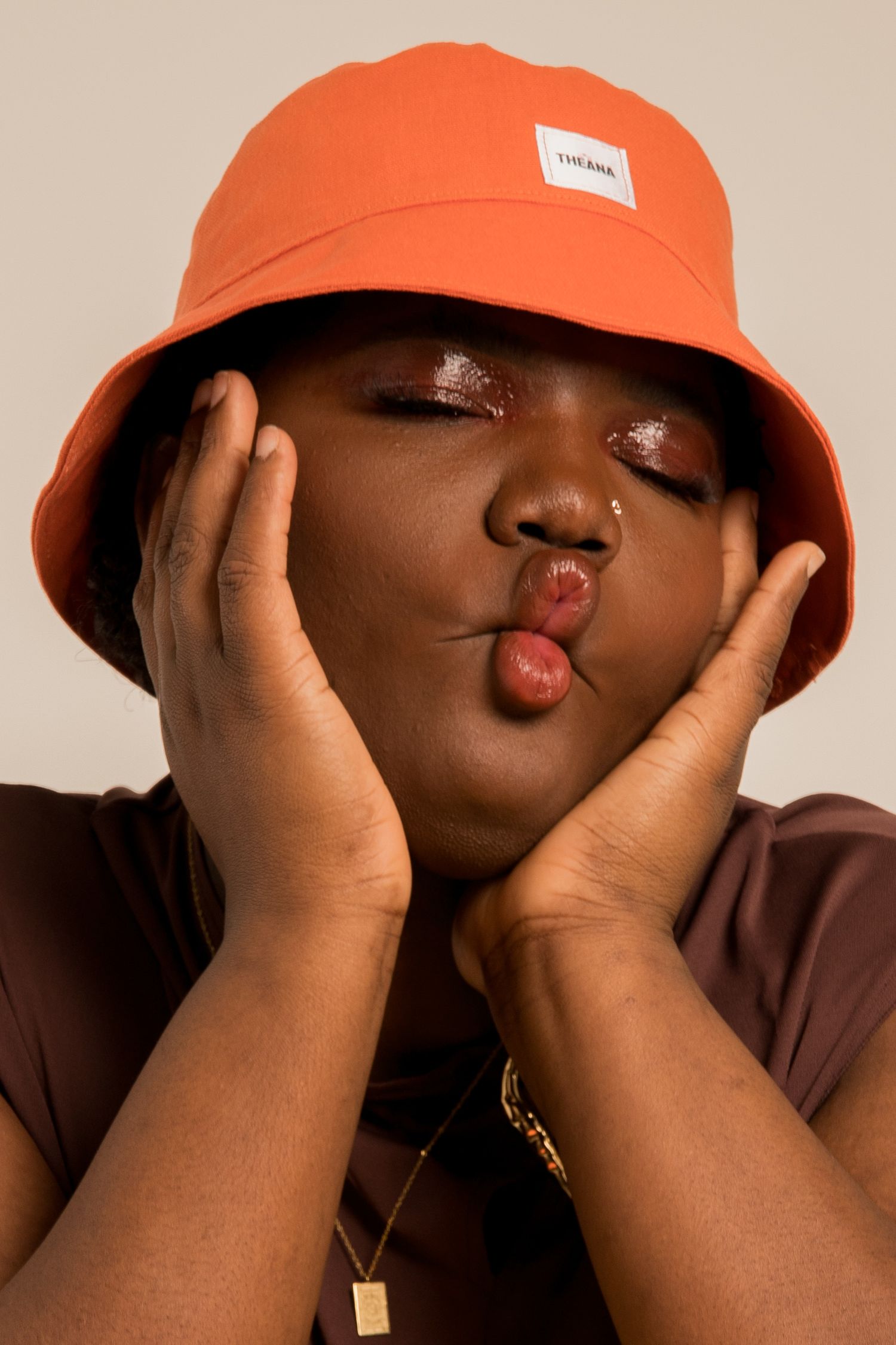 Close-up of woman blowing a kiss wearing an orange bucket hat with hands framing her face.