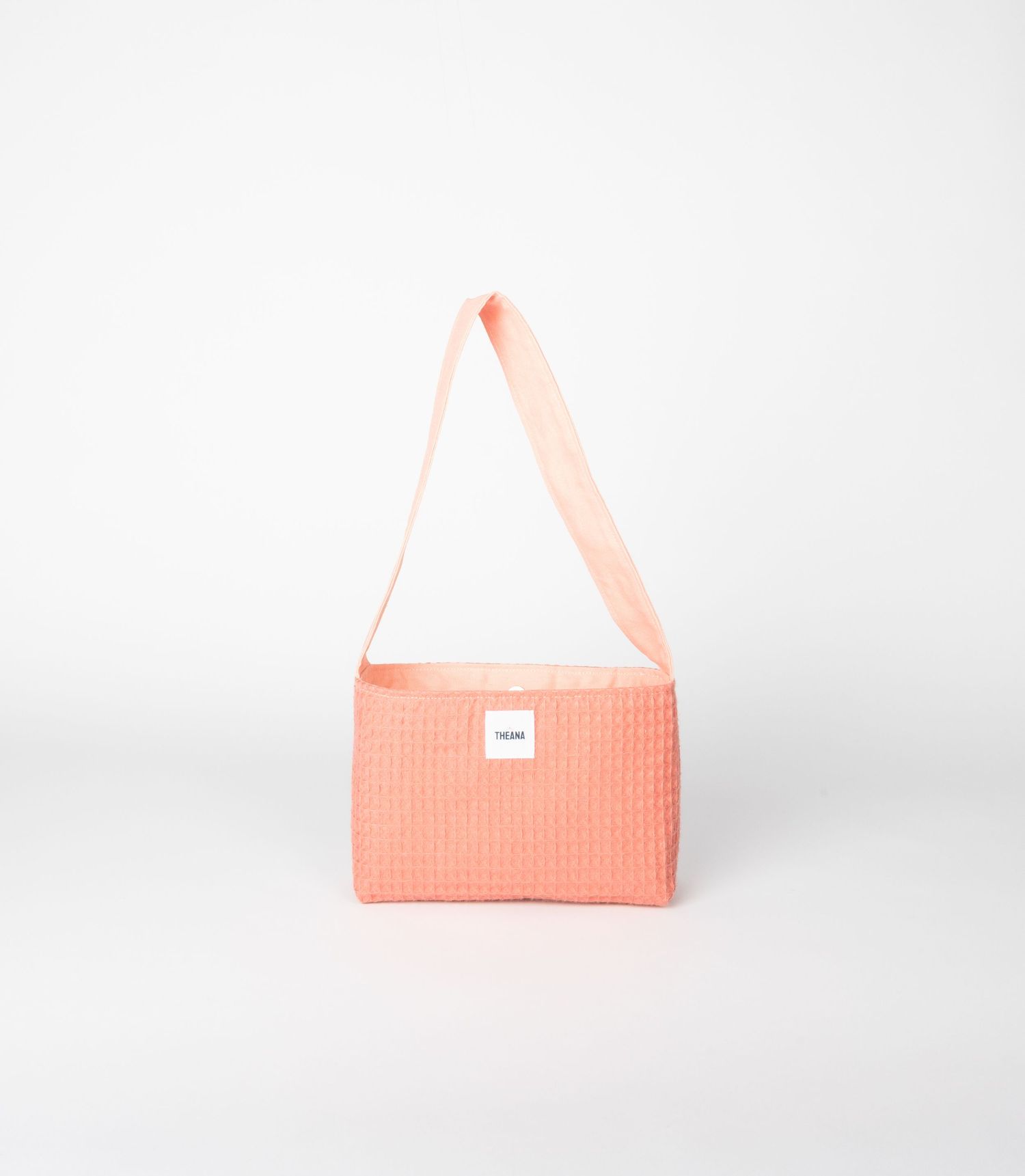 Peach coral quilted waffle-texture shoulder bag with matching long strap and small white brand label.