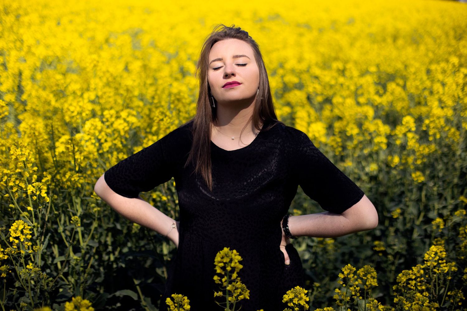 Young woman in black dress with eyes closed posing peacefully in a yellow rapeseed field.