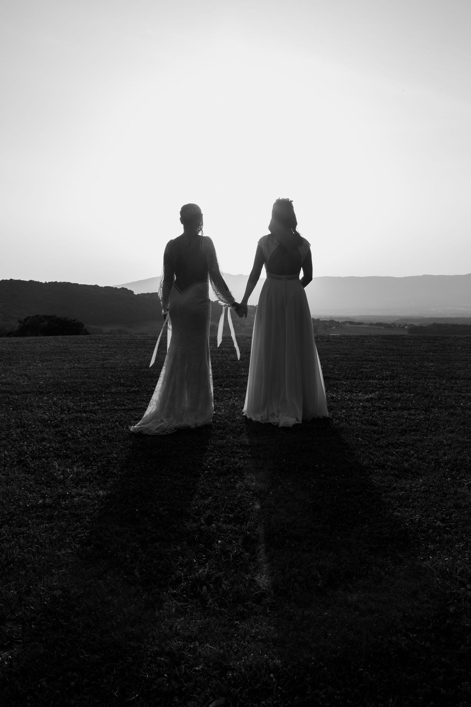 Silhouette of two brides holding hands in a field at sunset in black and white.