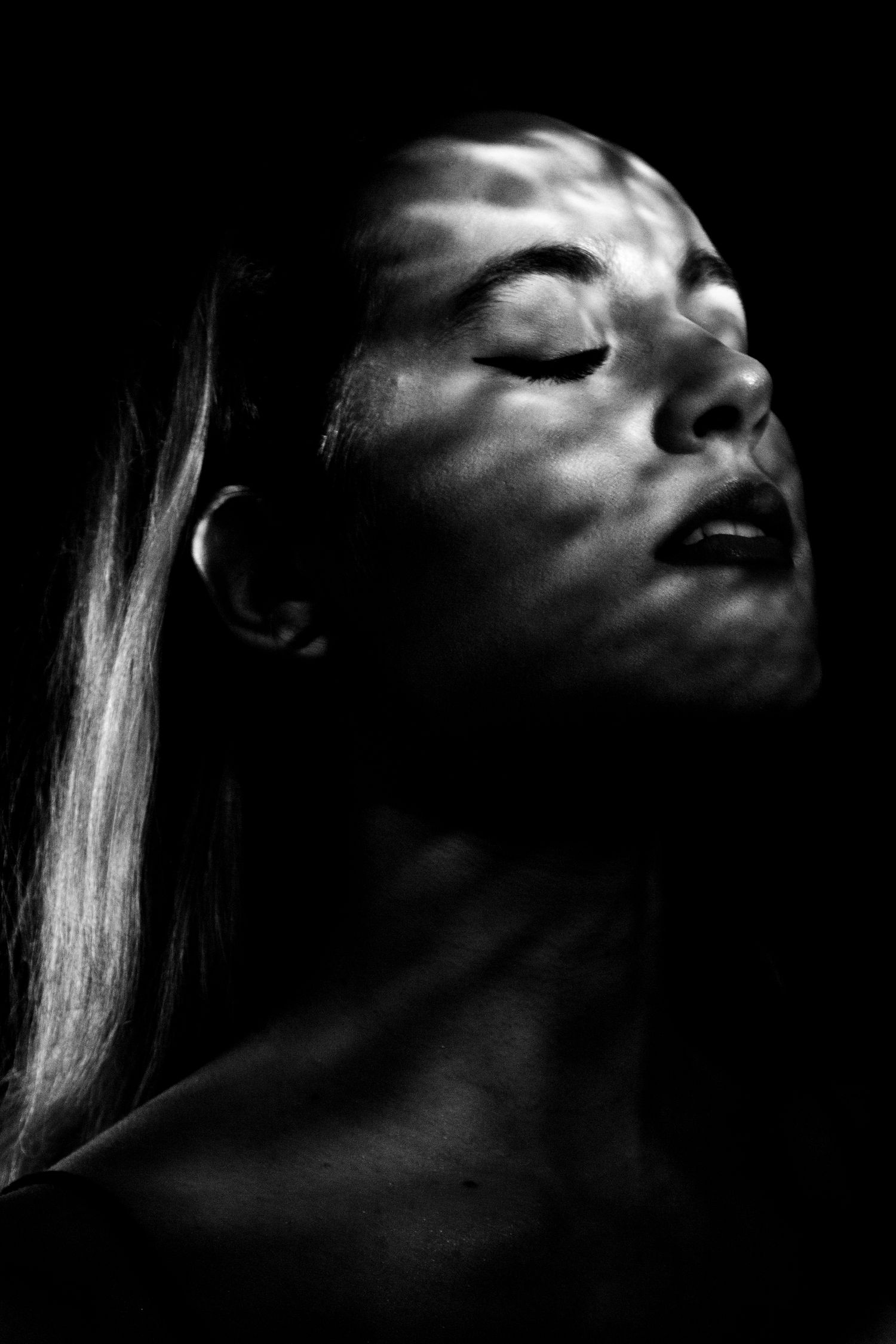 Black and white portrait of a woman with closed eyes and dappled light pattern projected across her face.