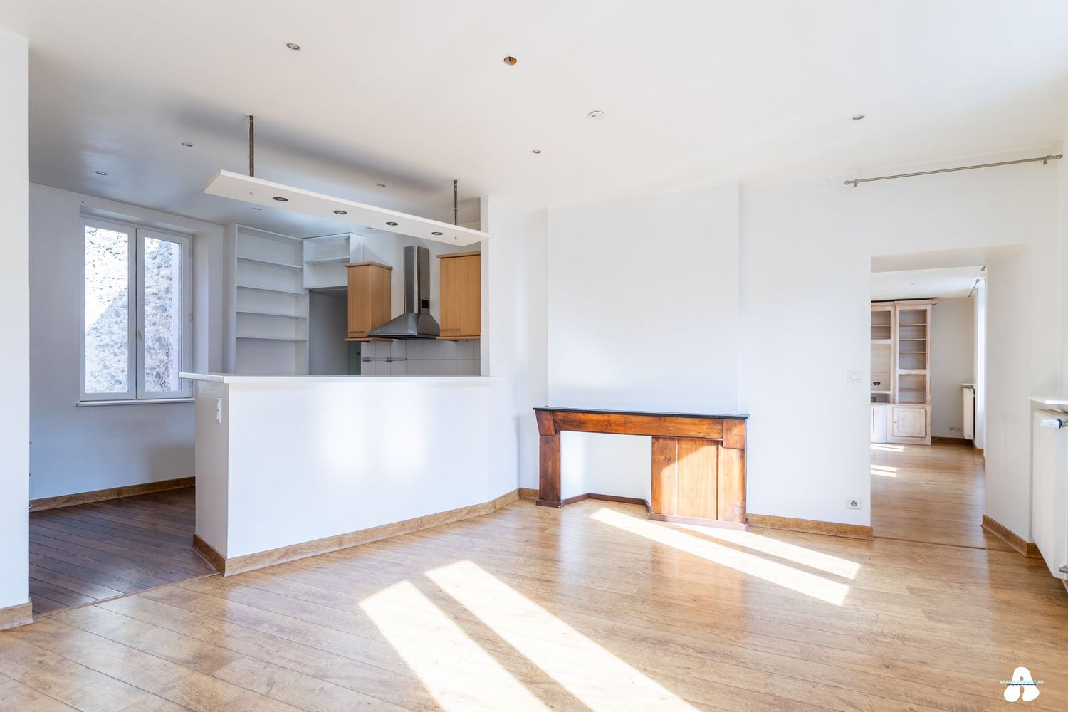 Open plan living space with kitchen peninsula, fireplace, and light hardwood flooring.