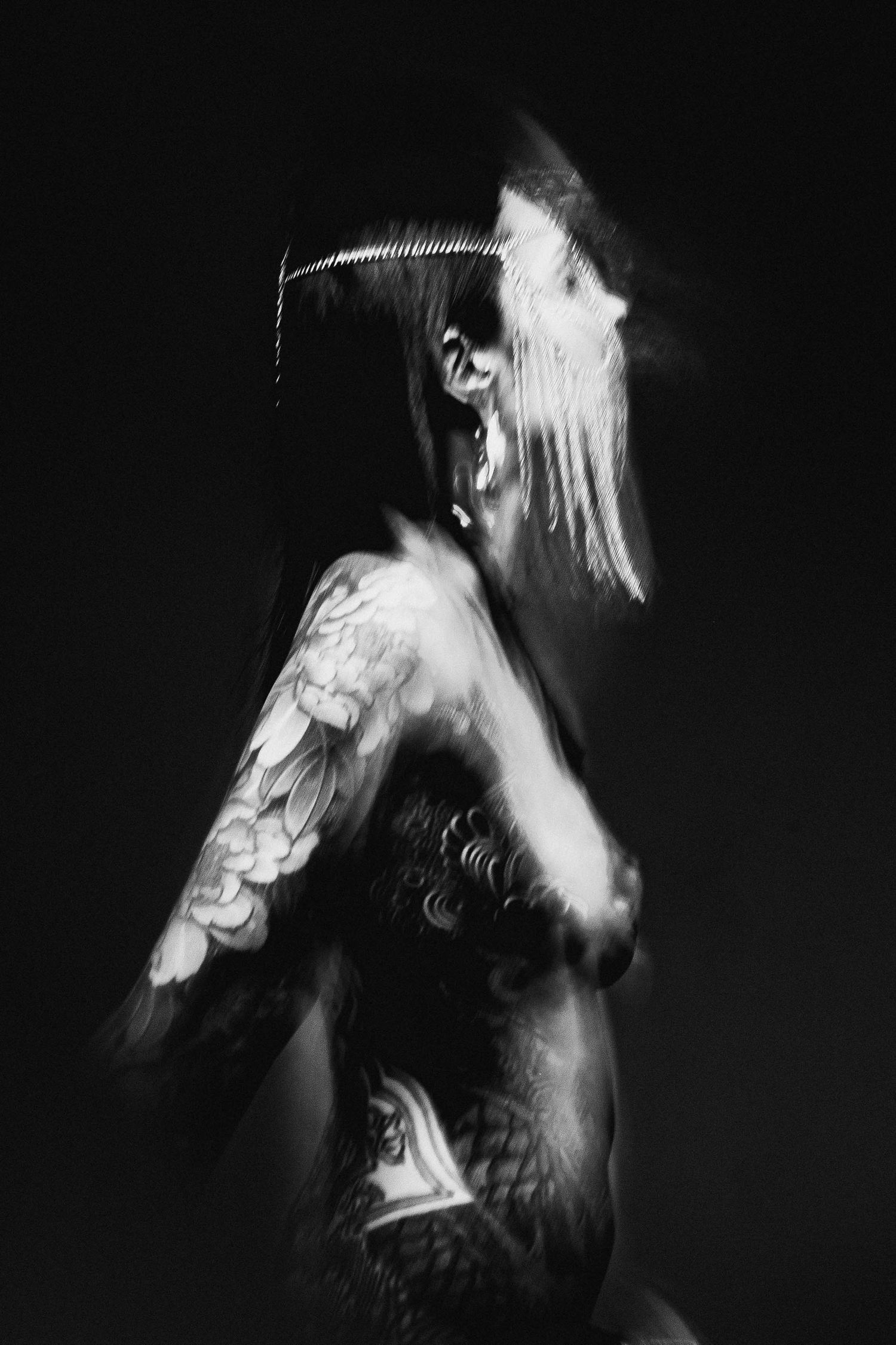Black and white long exposure portrait of tattooed woman with motion blur against dark background.