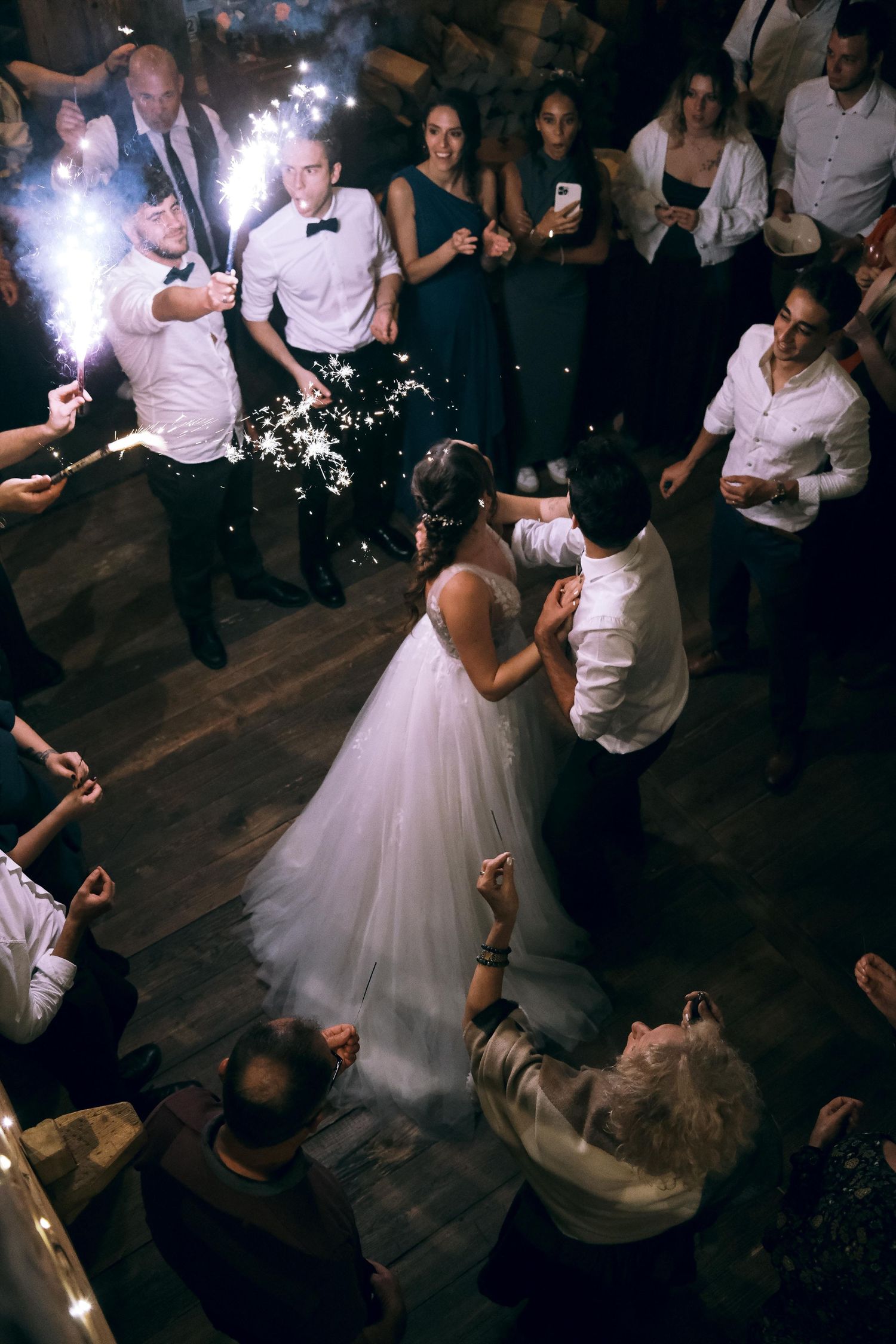 Bride and groom sharing first dance surrounded by sparkler-holding guests in a barn.