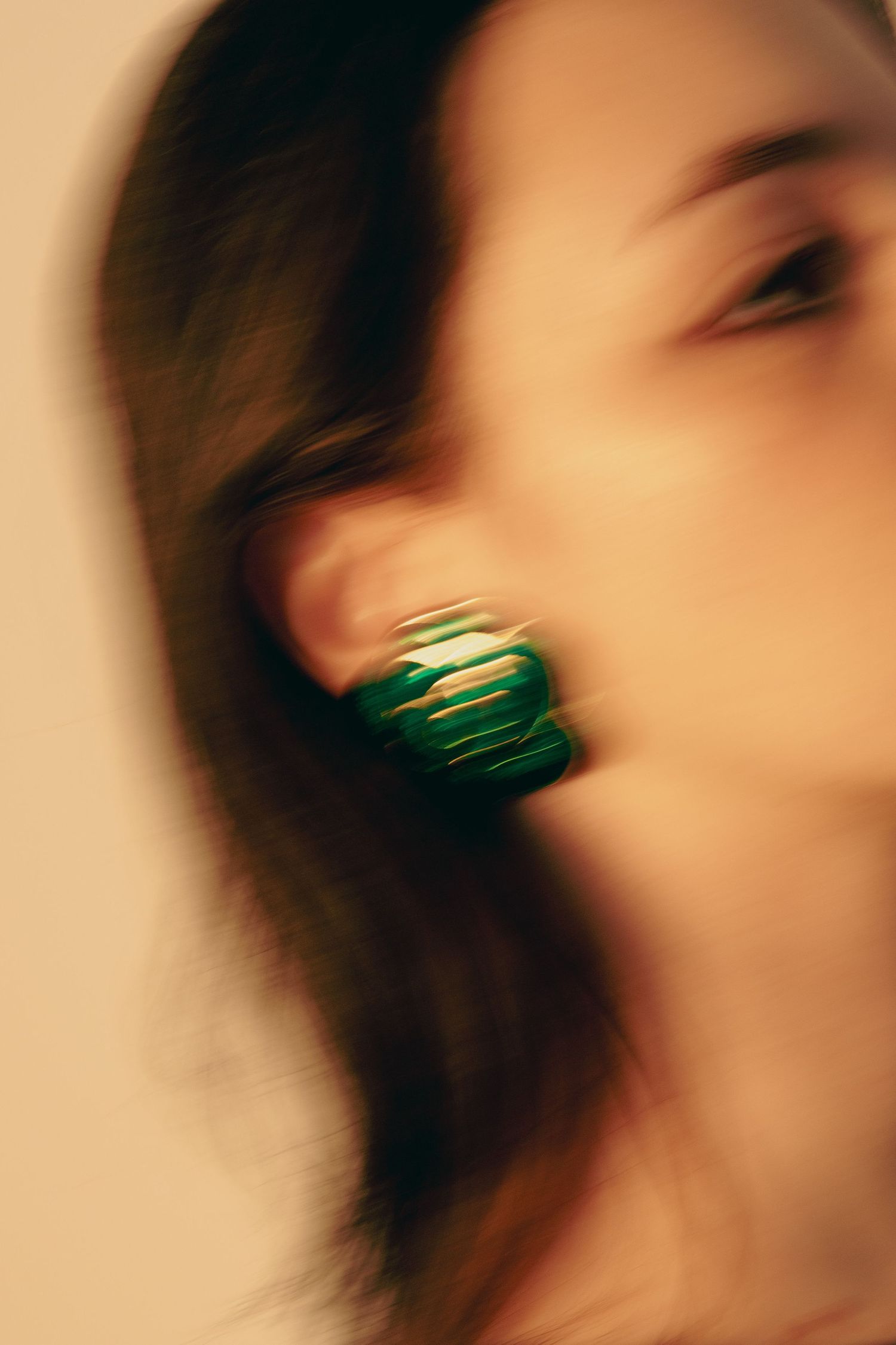 Close-up blurred artistic shot of large green chunky earring on dark-haired woman.