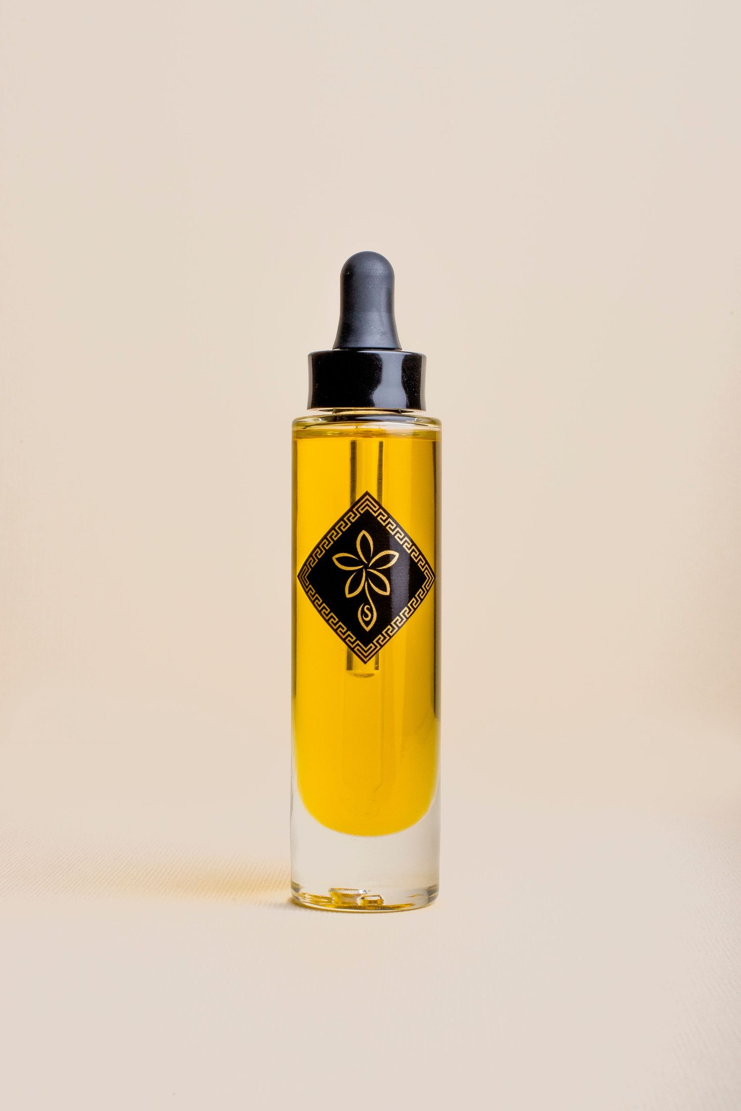 Elegant dropper bottle filled with golden facial oil featuring black diamond logo on beige background.