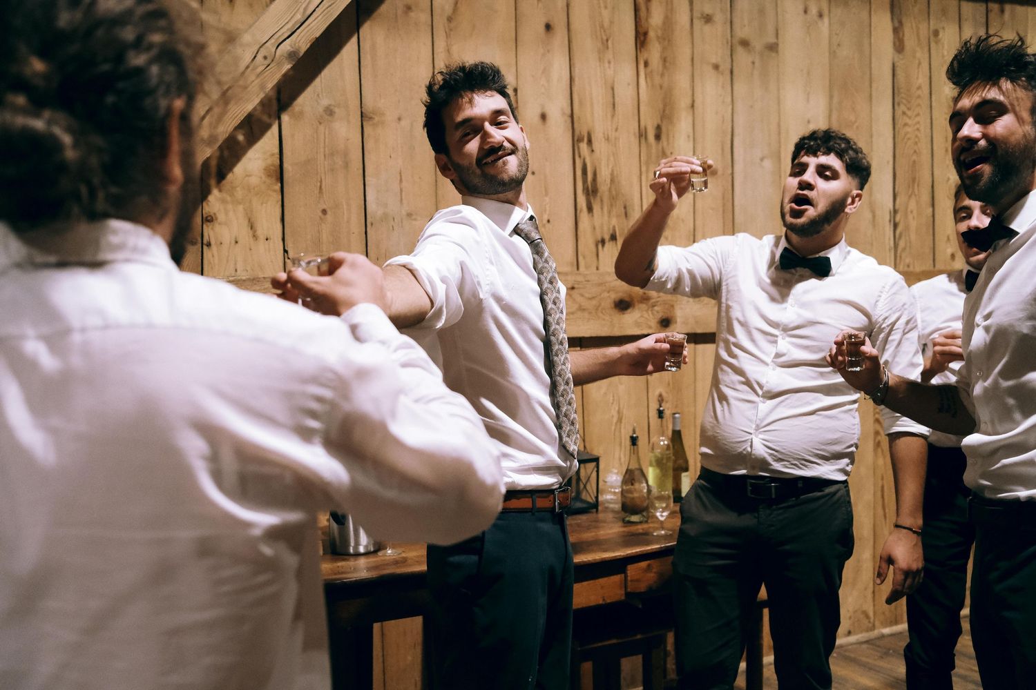 Cheerful group of men in white shirts dancing and laughing together at a rustic barn wedding party.
