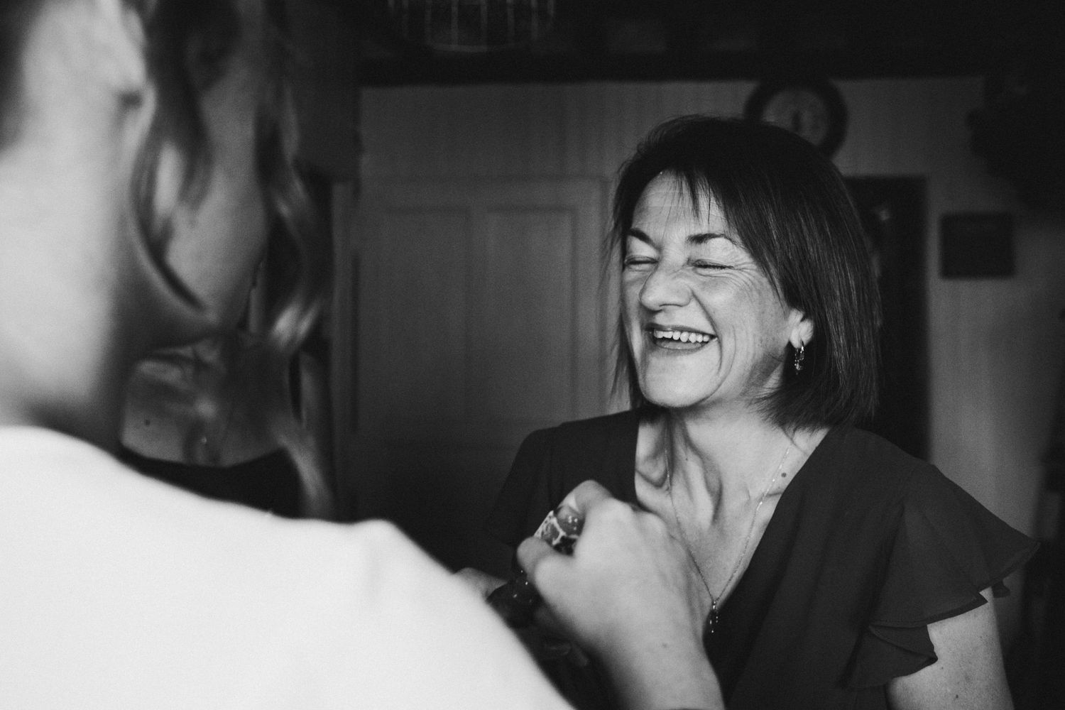 Black and white candid photo of a woman laughing joyfully during a conversation in a cozy indoor setting.