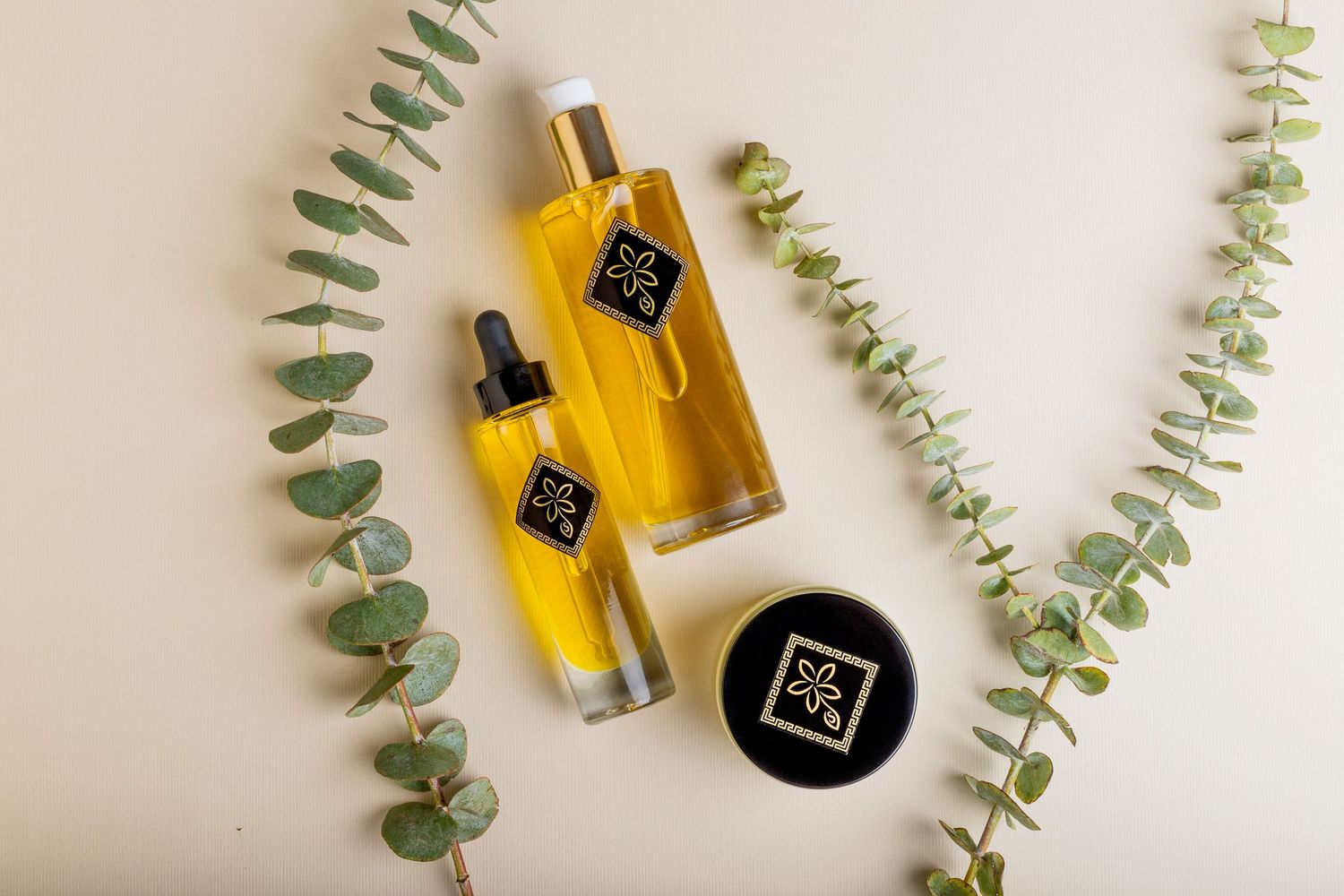 Two golden oil bottles and cream jar with eucalyptus branches on white flat lay background.