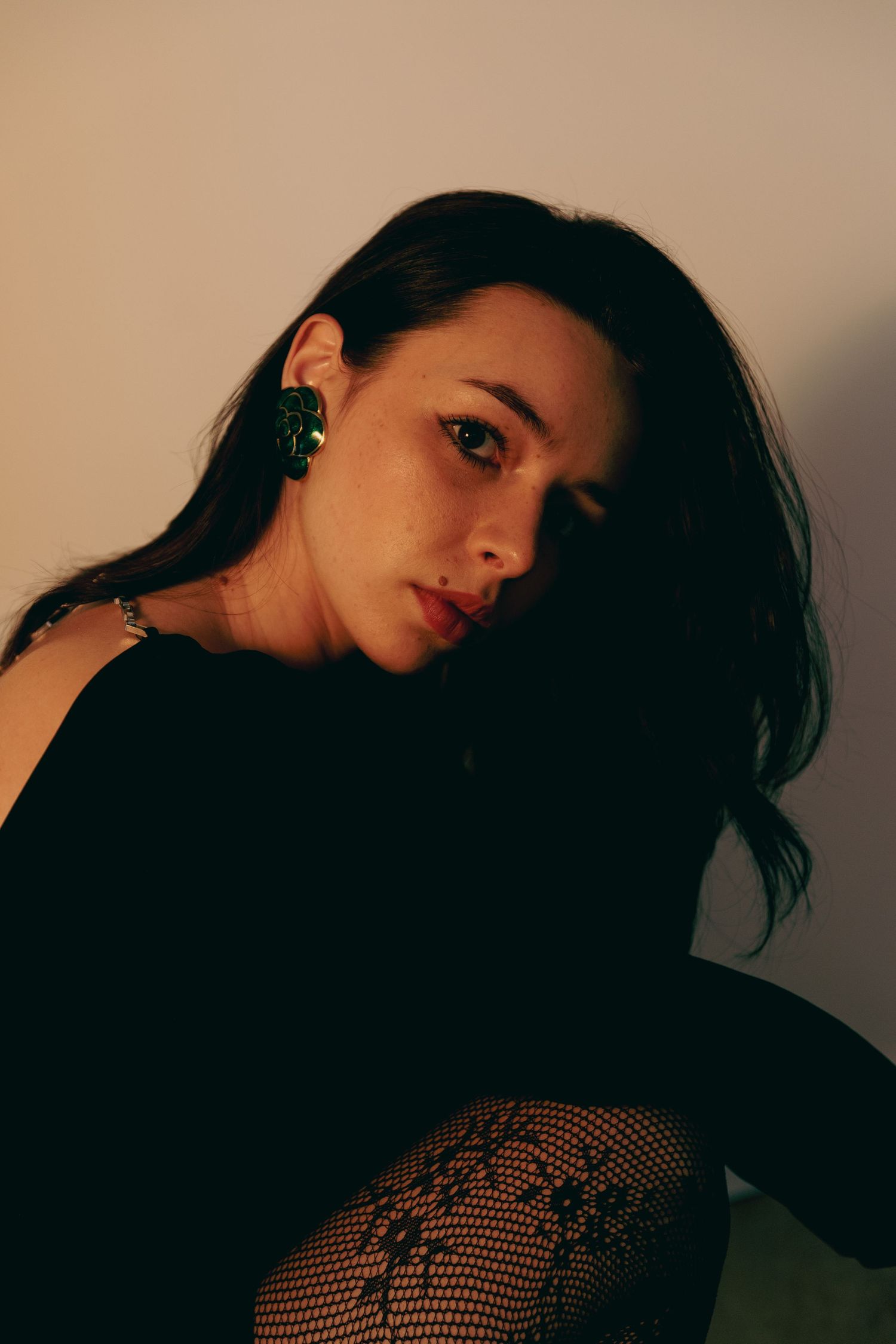 Woman with green earrings in black top posing with dramatic warm side lighting.