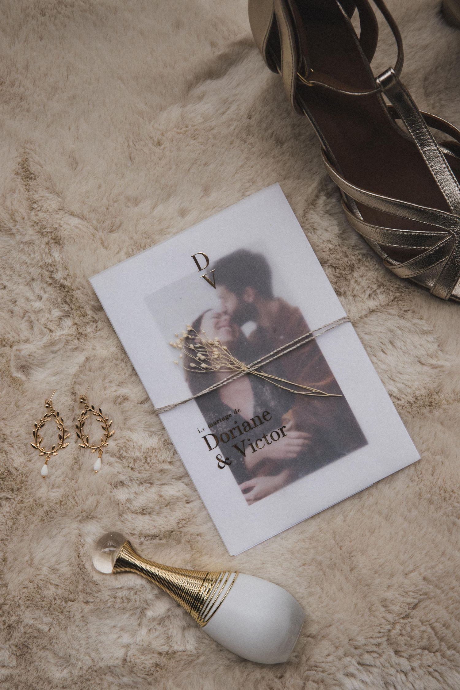 Wedding invitation for Doriane and Victor displayed with gold earrings, perfume bottle and heels on fur.