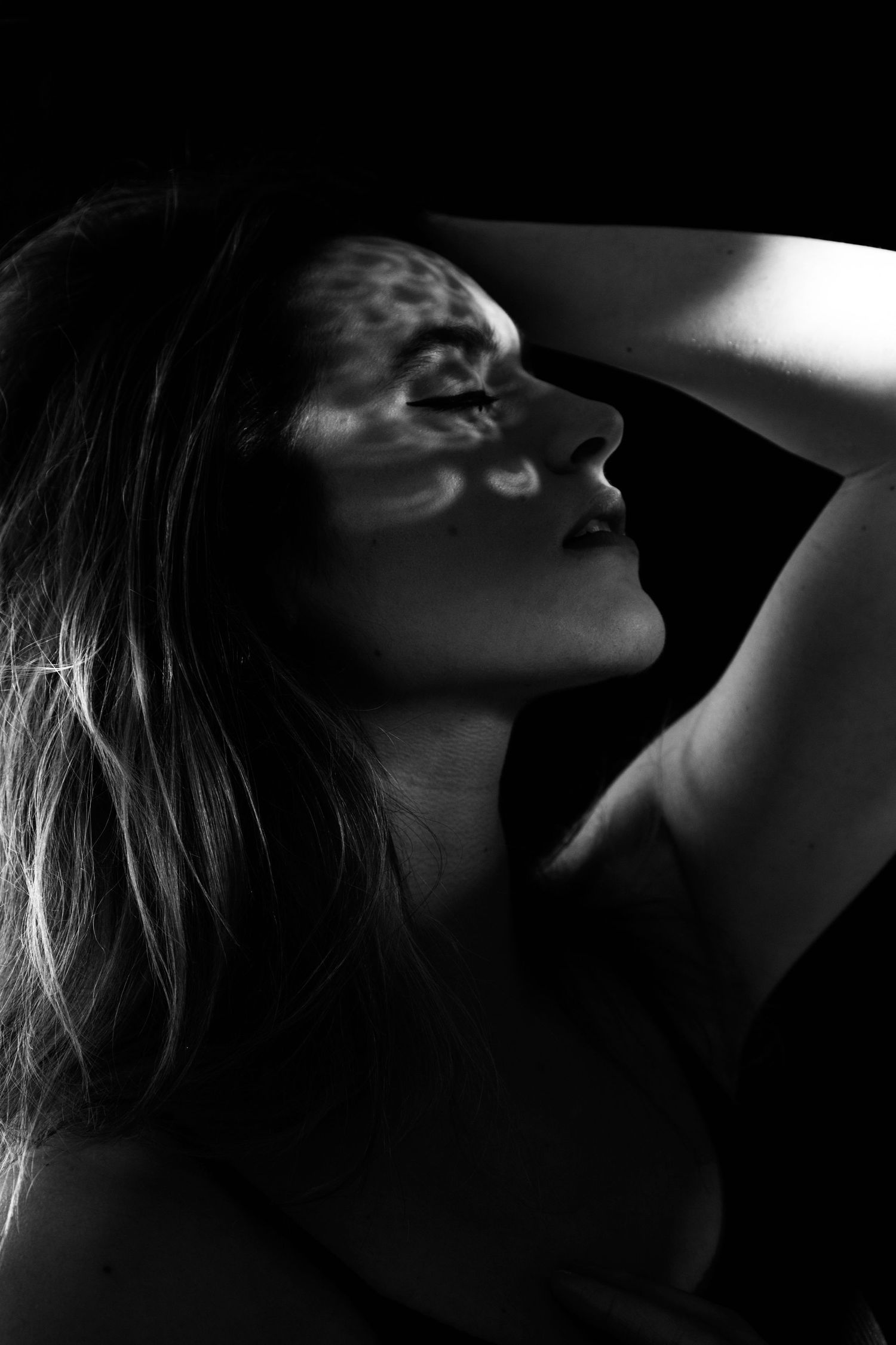 Artistic black and white silhouette of a young woman with eyes closed and arm raised above her head.