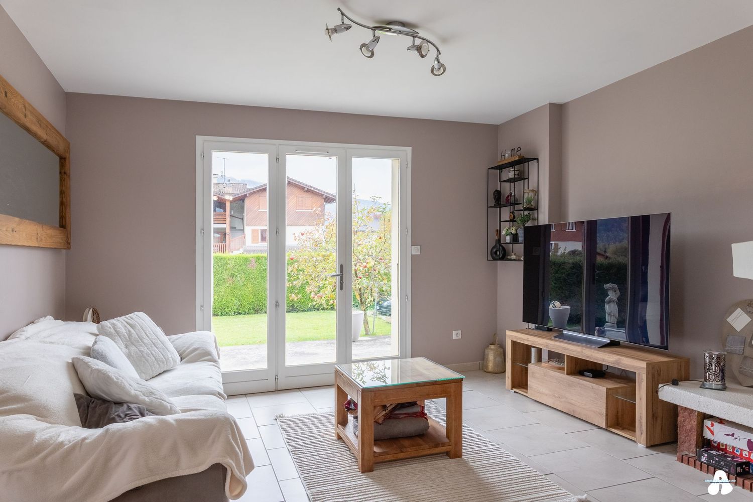 Cozy living room with white sofa, glass coffee table, TV unit and French doors to garden.