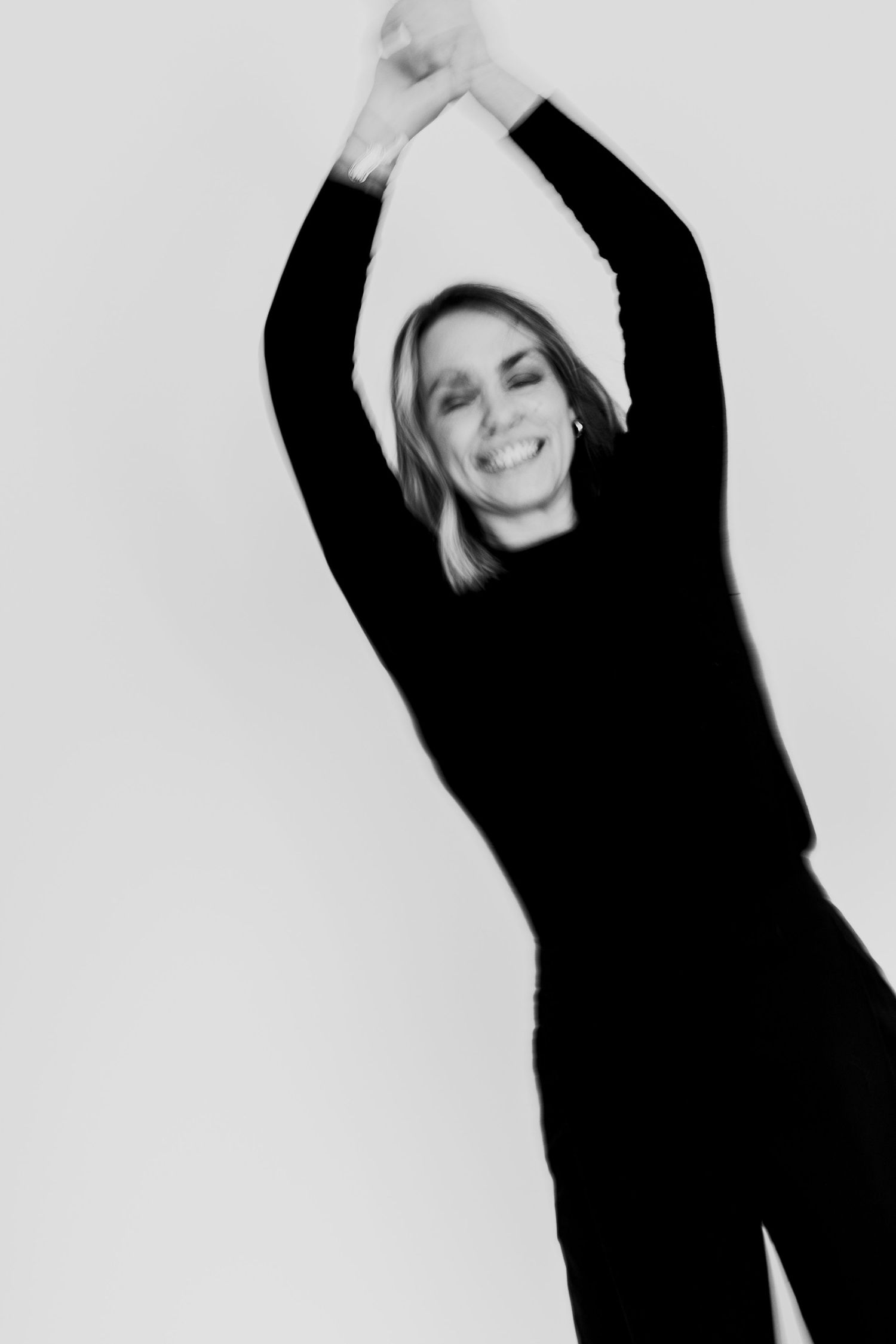 Blurred motion black and white photo of woman in black raising arms overhead.