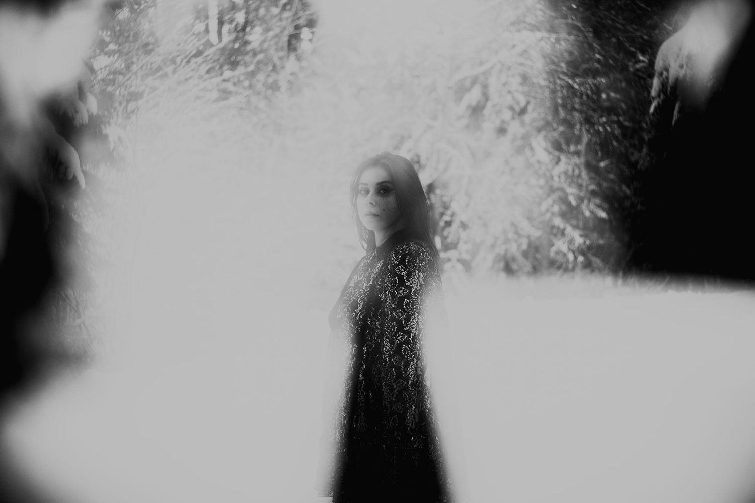 Black and white ethereal portrait of a woman in lace standing in a bright misty forest.
