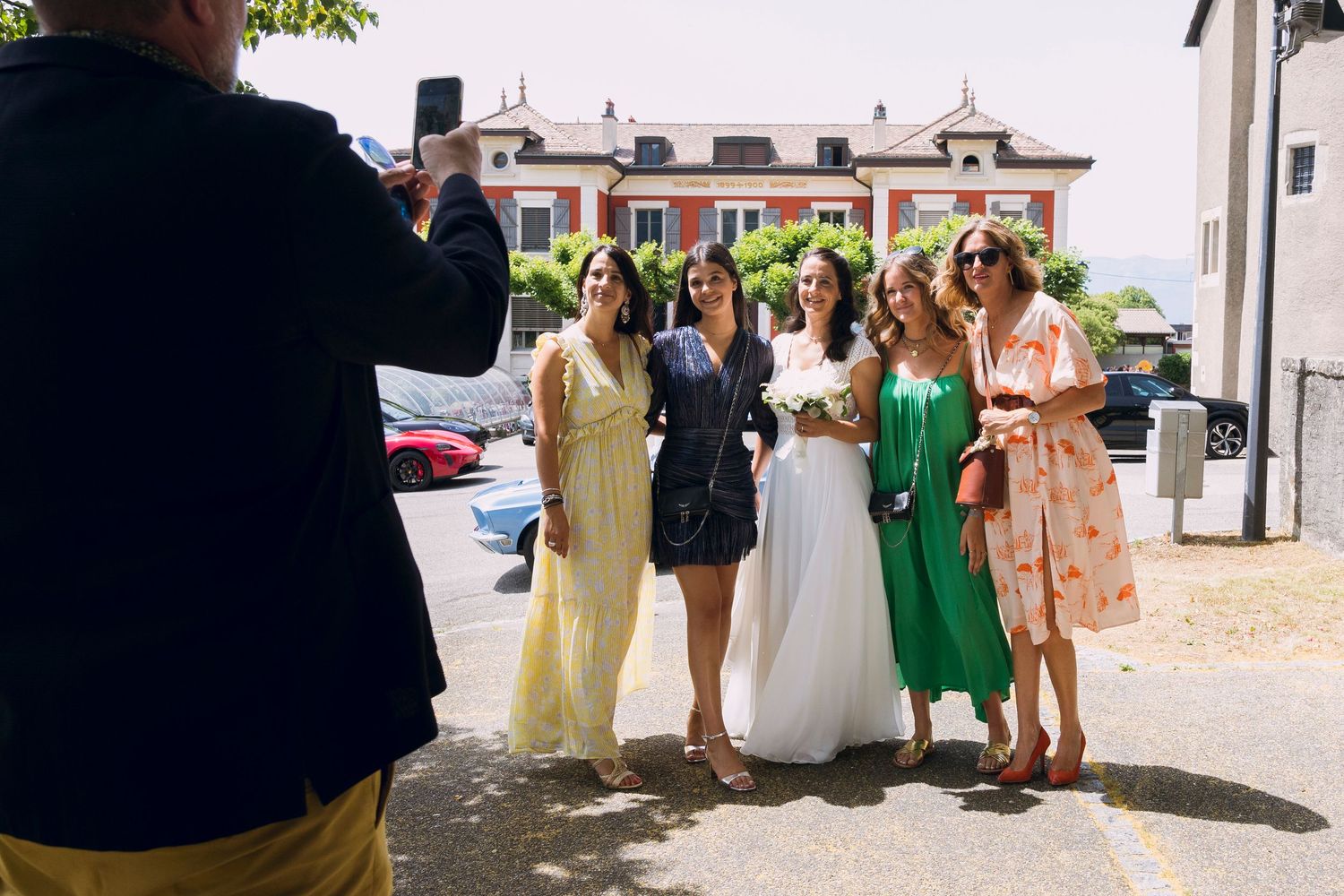 Group of women in colorful dresses posing for a photo outside at a wedding celebration on a sunny day.