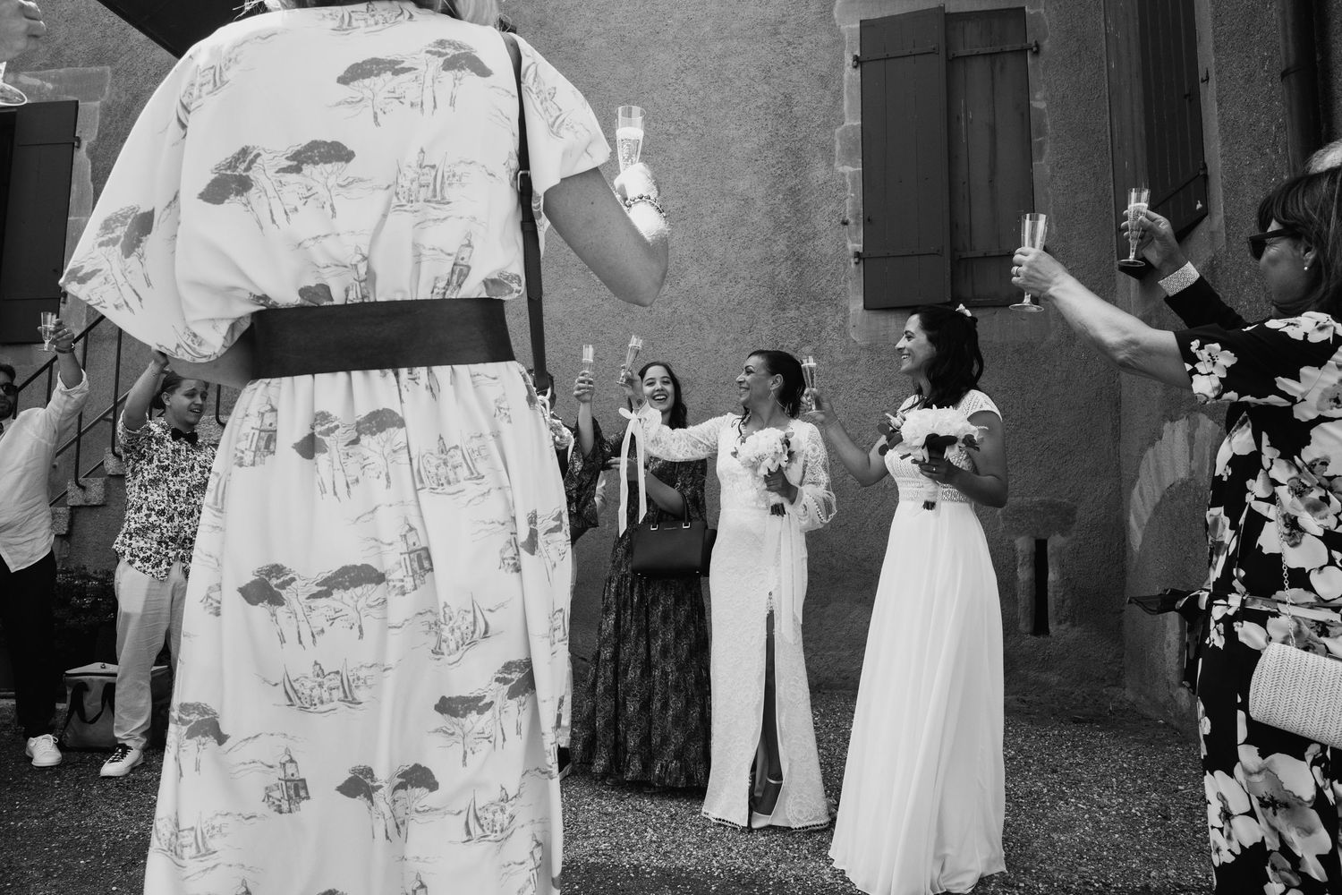 Black and white photo of two brides celebrating with guests raising glasses at a wedding reception.