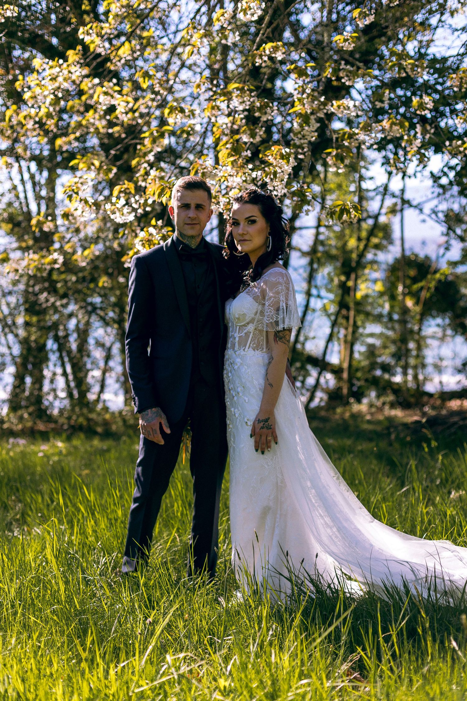 Bride and groom pose together under blooming cherry blossom tree in sunny garden.