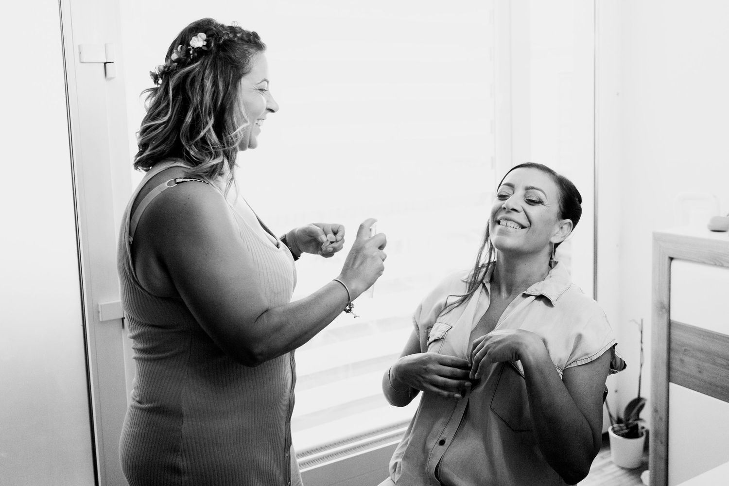 Black and white photo of two women laughing together during bridal wedding preparations.