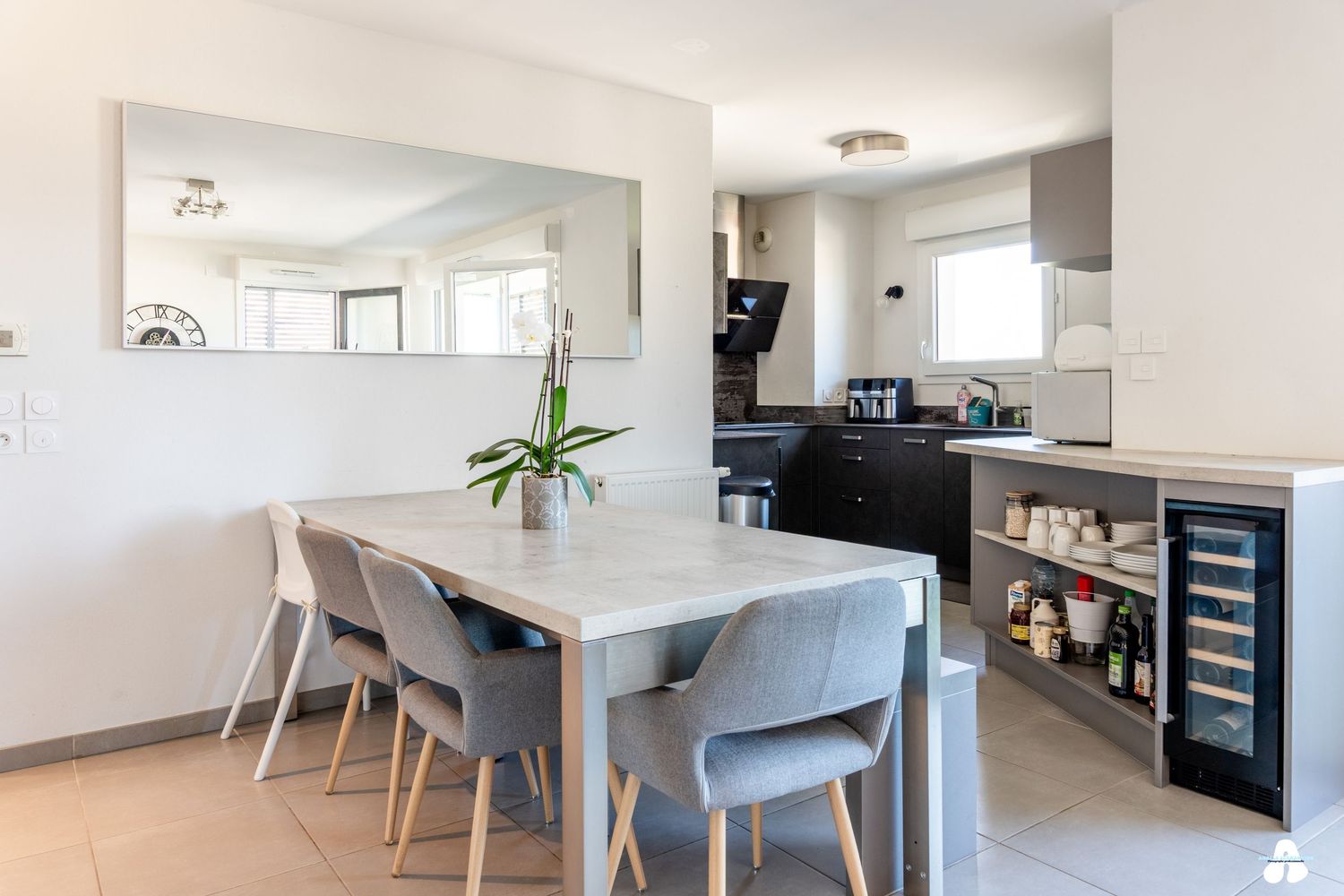 Contemporary dining area with large mirror, wine cooler, and dark kitchen cabinets.