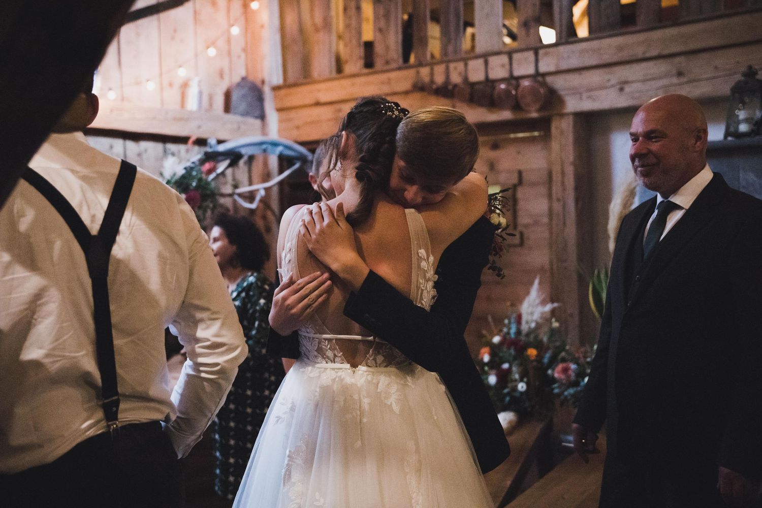 Bride in white tulle gown shares emotional hug with guest in rustic barn reception.
