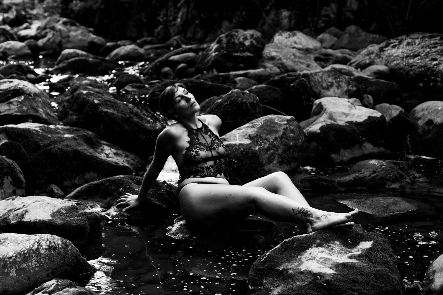 Woman in swimsuit reclining on rocks by a stream, black and white nature photography.