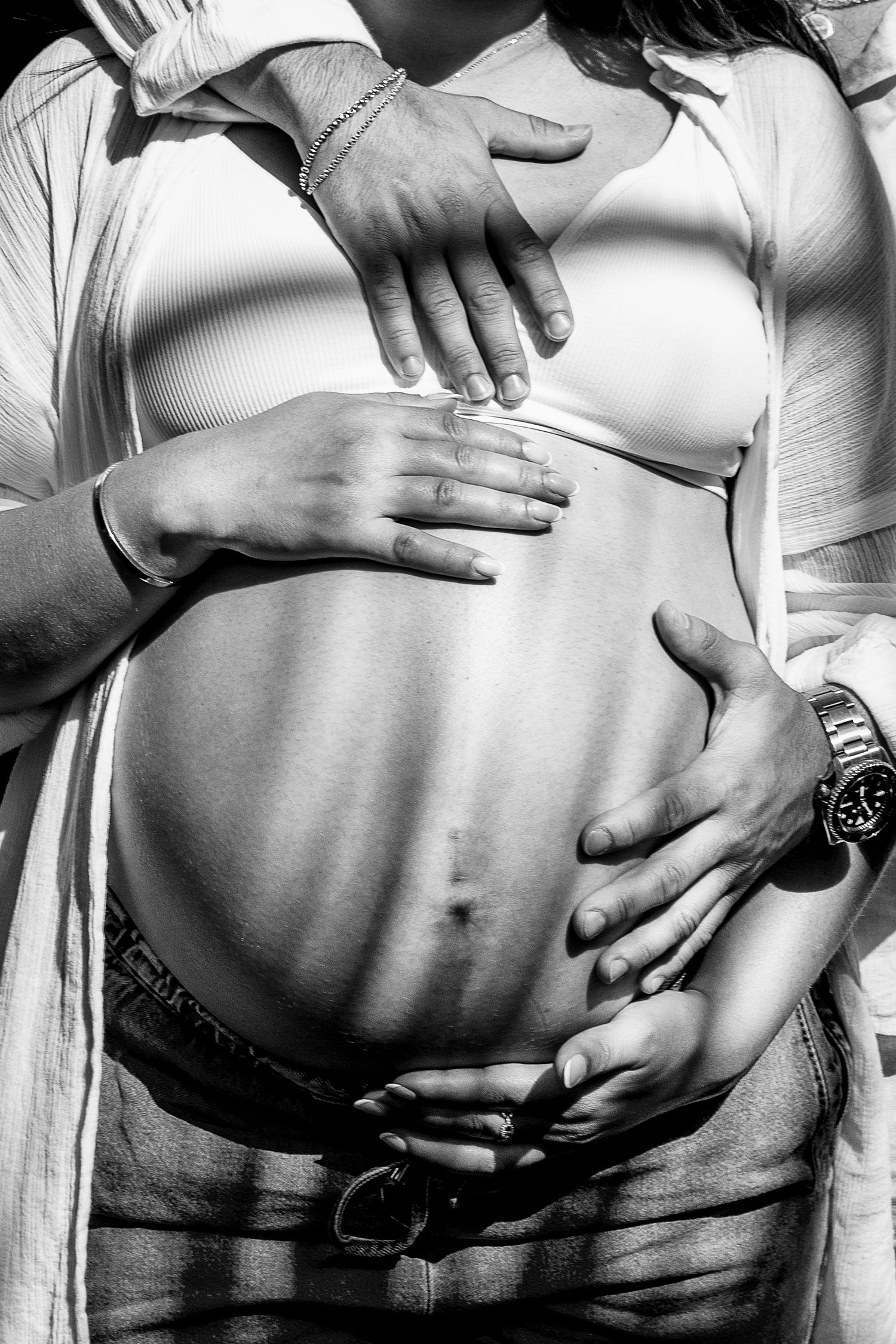 Close-up black and white photo of couple's hands cradling pregnant belly in tender maternity portrait.