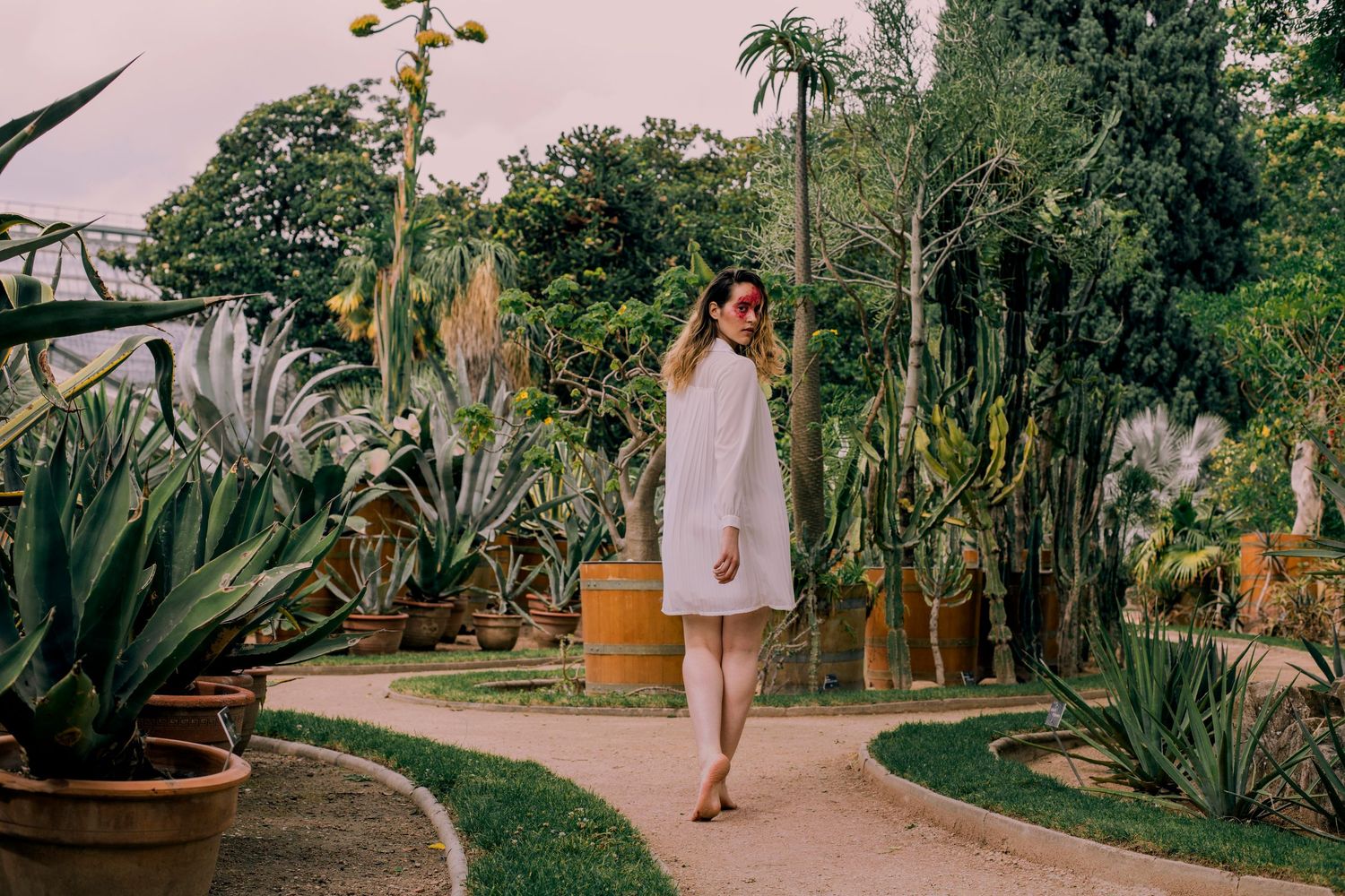 Woman in white dress walking through a botanical garden with cacti.