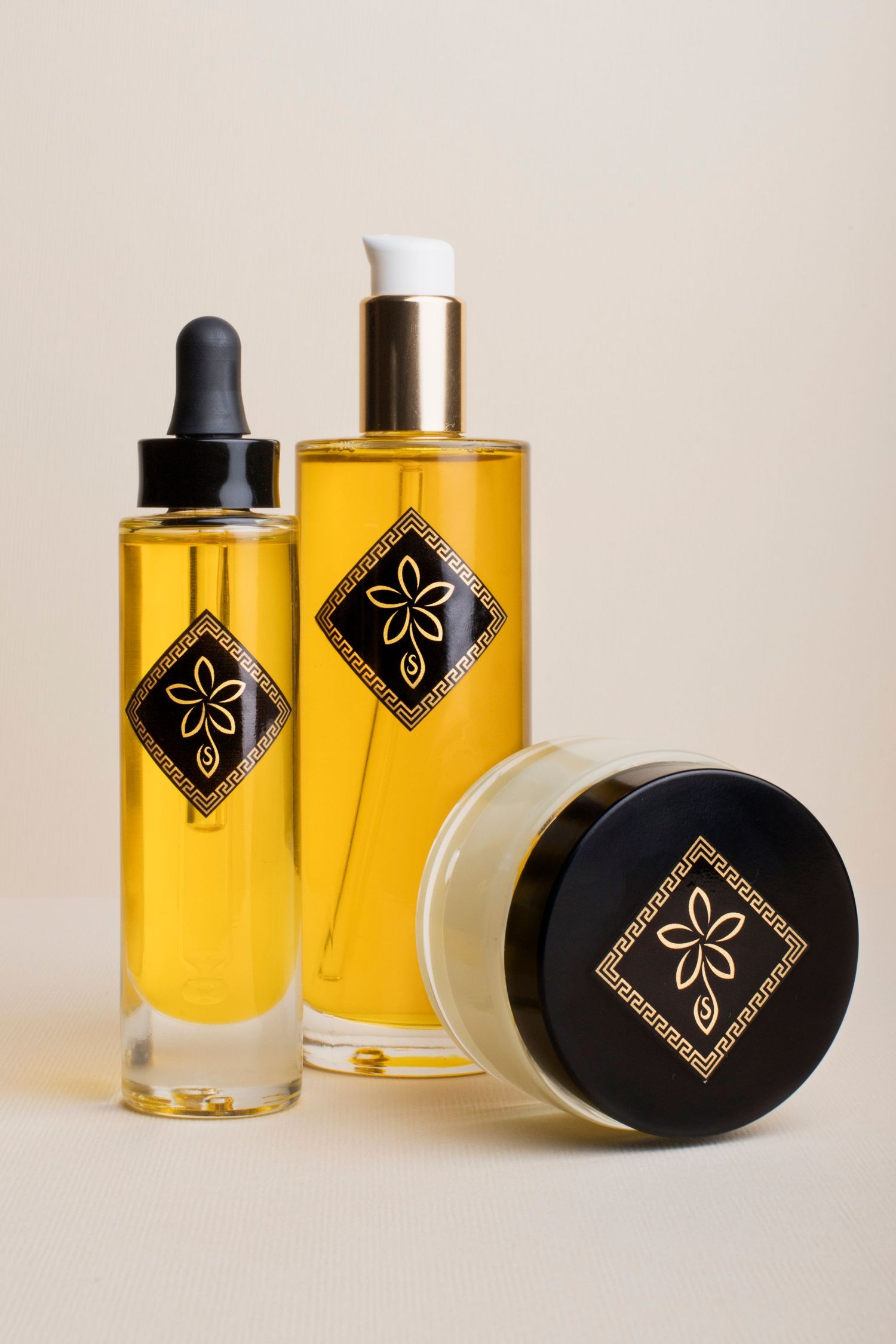 Three luxury skincare products with gold diamond labels arranged on a neutral beige background.