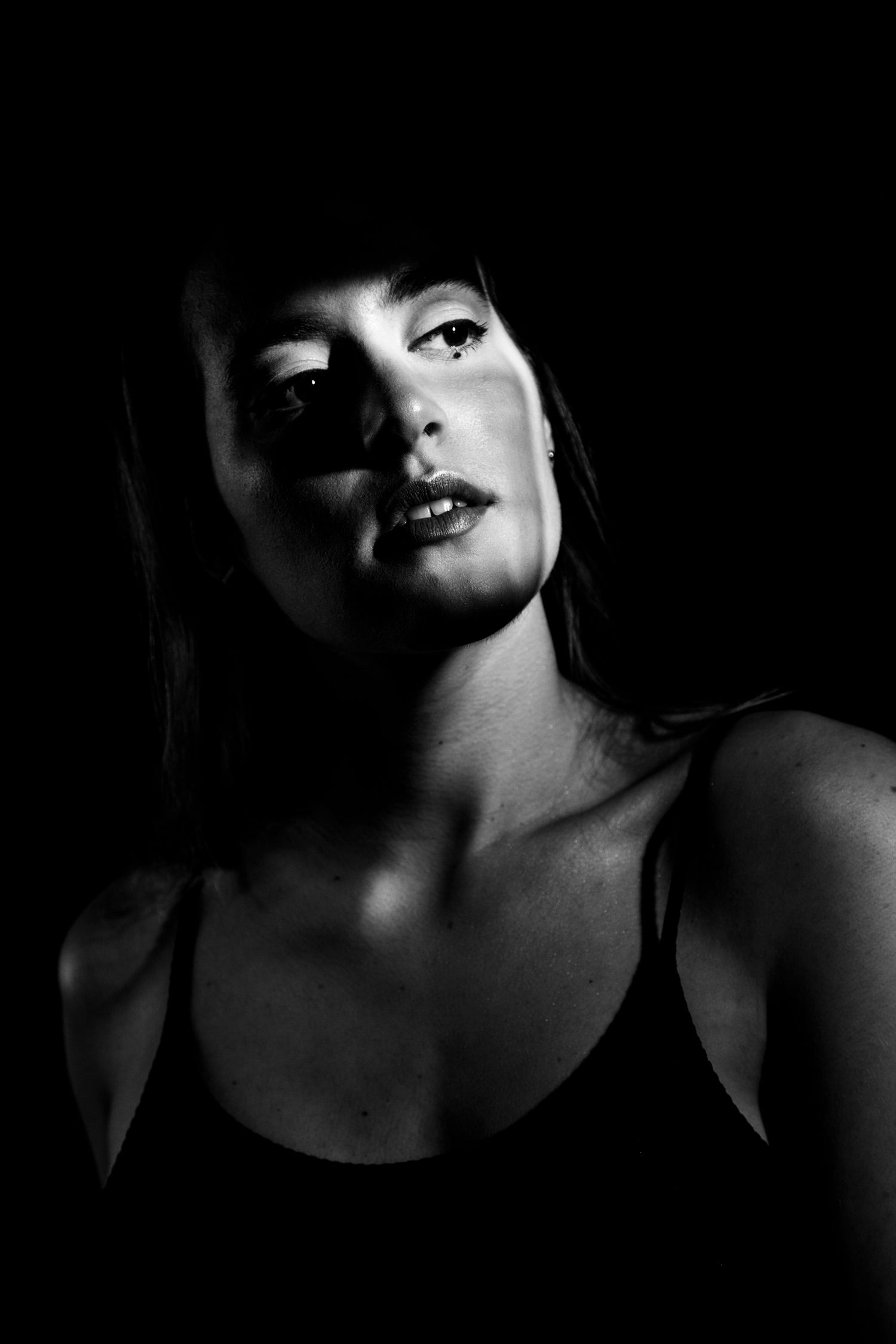 Dramatic black and white low-key portrait of a woman in tank top looking upward with moody lighting.