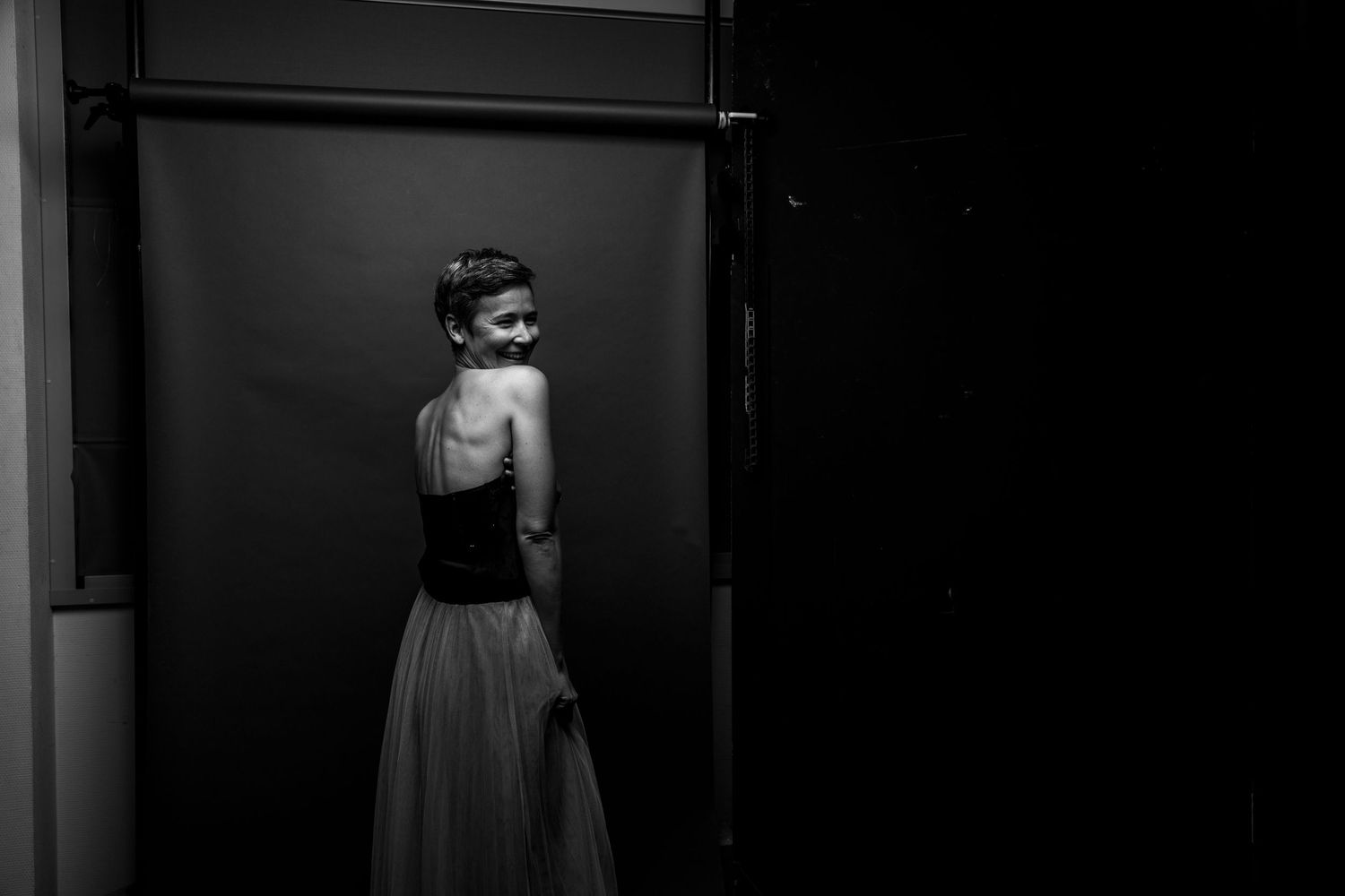 Woman in black top and white tulle skirt glancing back over shoulder in dark moody black and white photo.