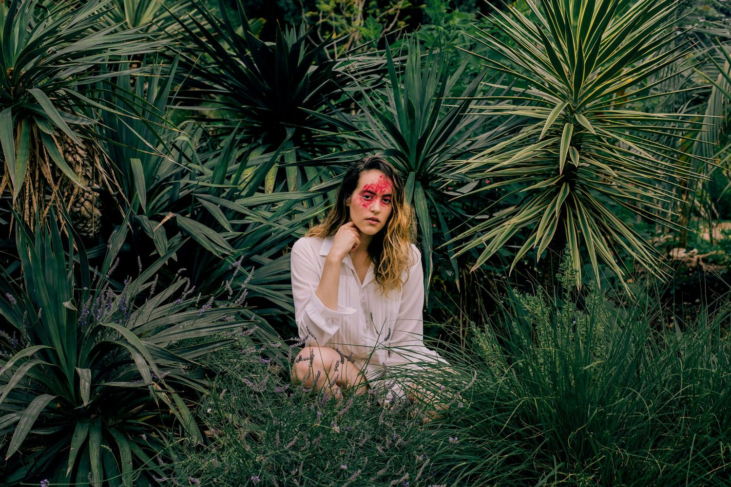 Woman with pink sunglasses sitting among lush tropical green plants.