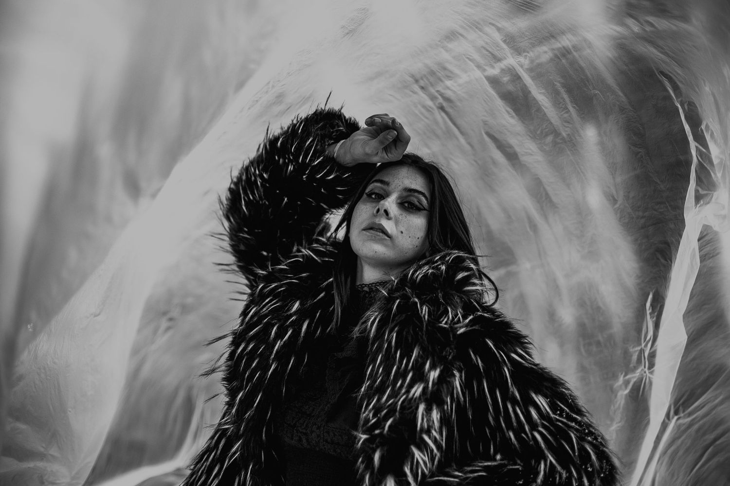 Dramatic black and white portrait of a woman in fur coat posing with translucent fabric.