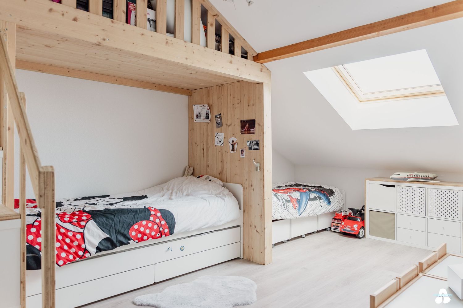 Cozy attic children bedroom with wooden bunk beds, skylight, and white storage drawers.