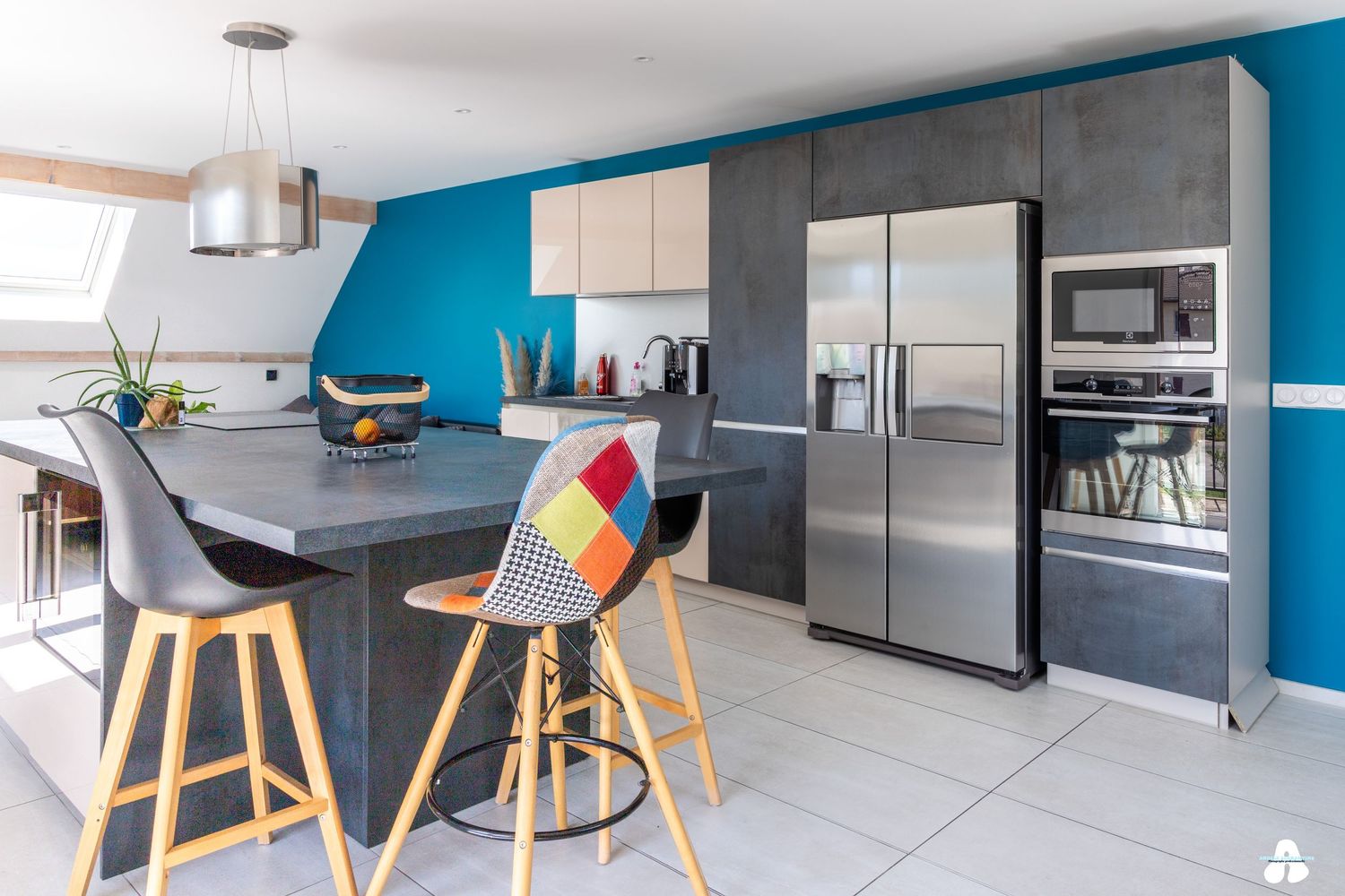 Modern kitchen with blue accent wall, gray island, colorful bar stools, and stainless steel appliances.