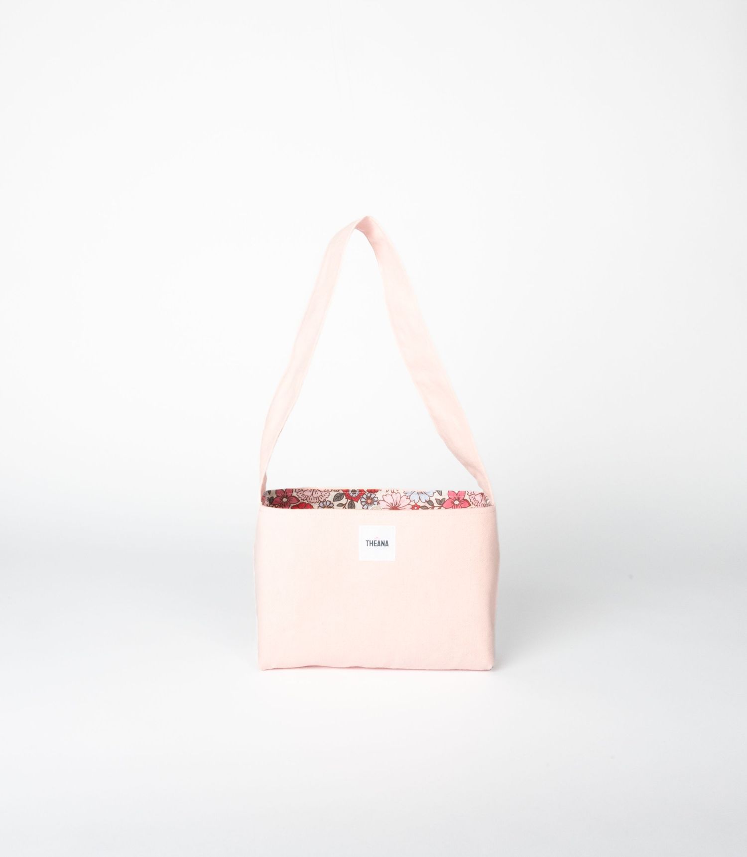 Light pink canvas shoulder bag with floral trim detail and long strap, minimalist design with small brand label.