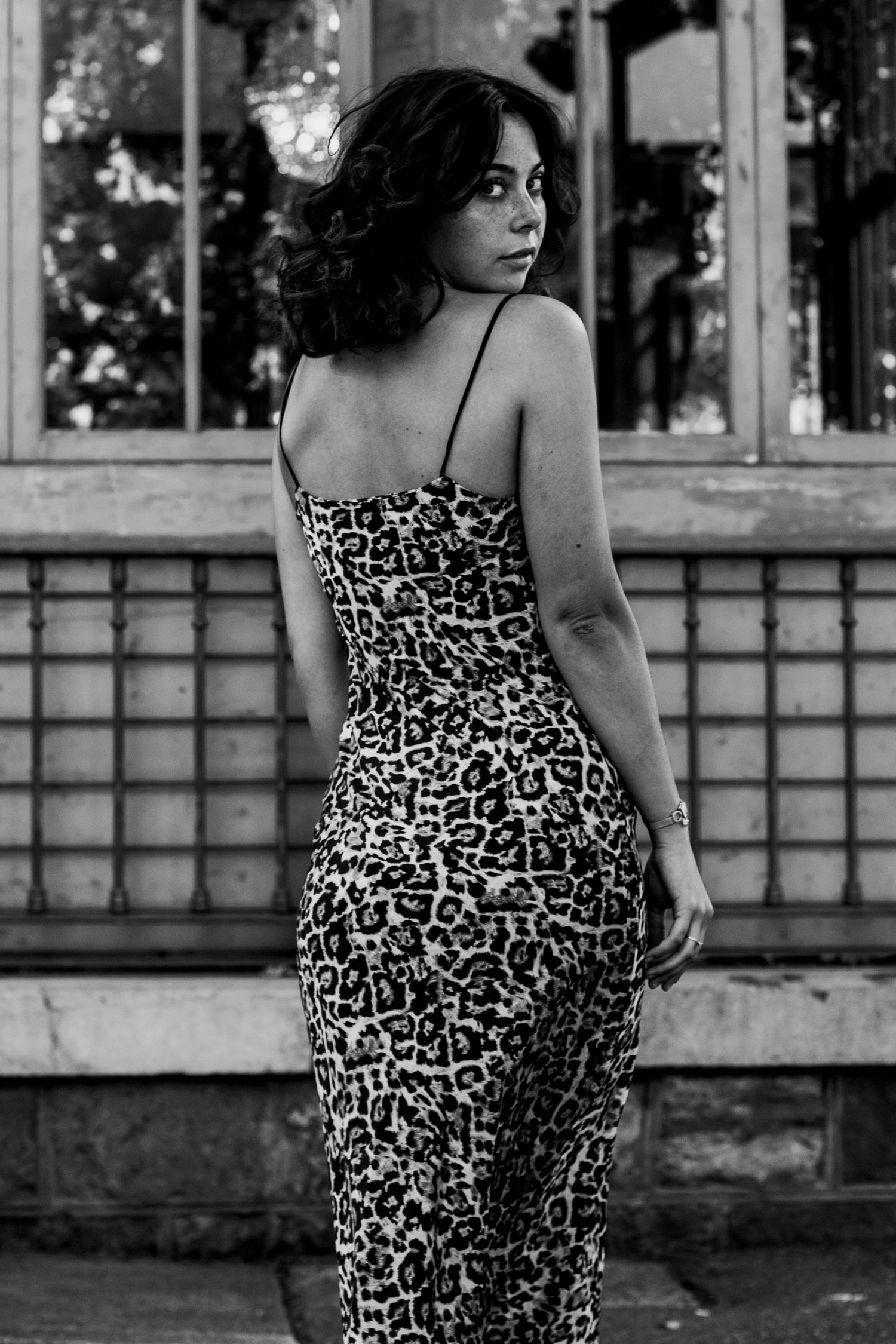 Black and white portrait of woman in leopard print dress with back turned near tiled wall.