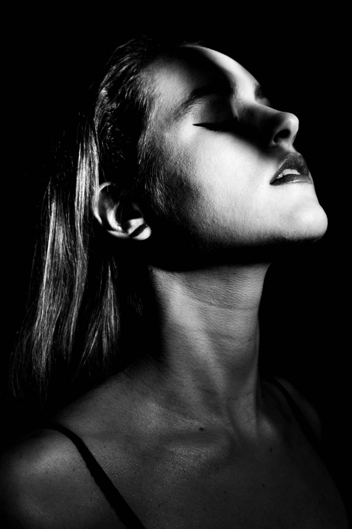 Black and white artistic portrait of a woman with head tilted back, eyes closed, dramatic side lighting.