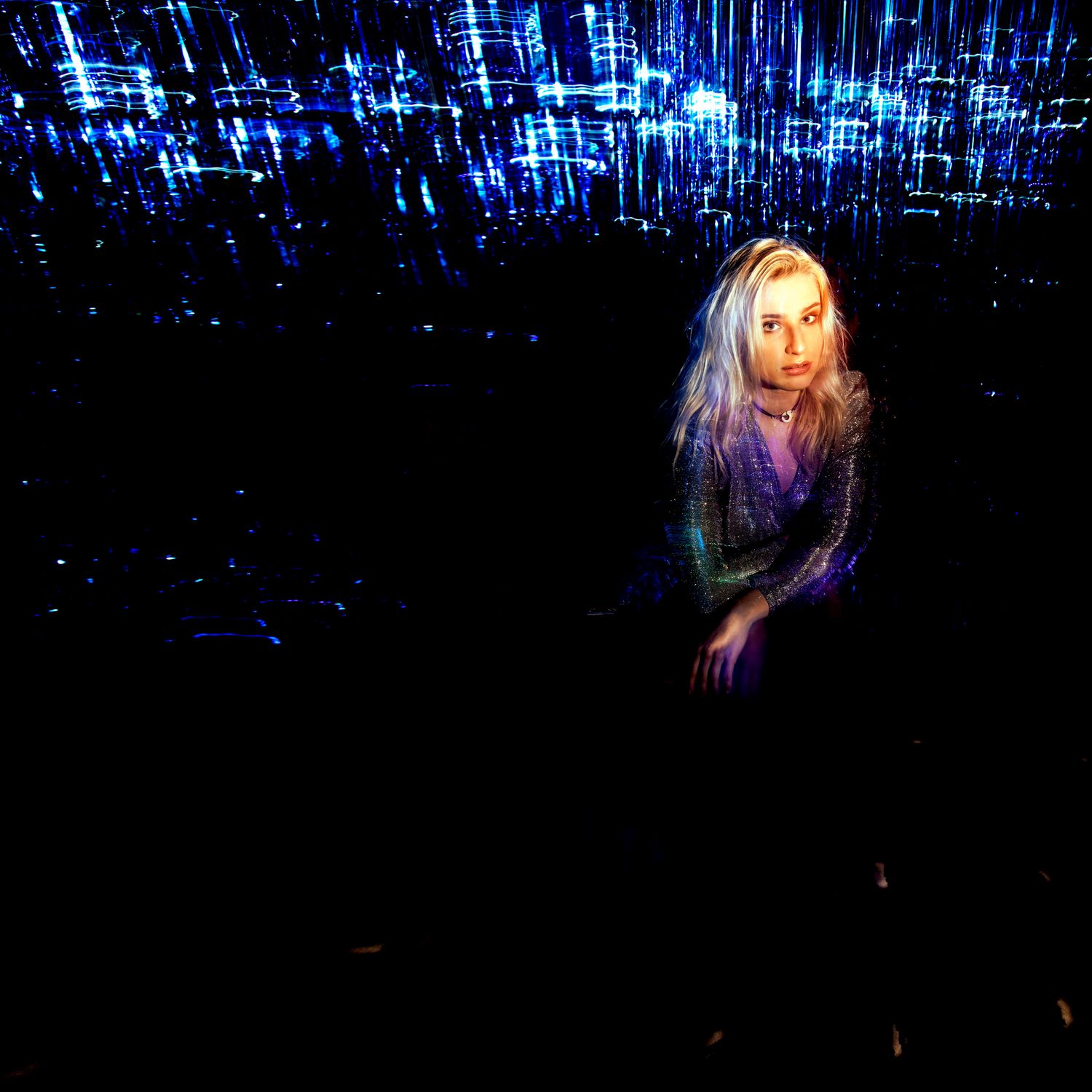 Blonde woman surrounded by blue light streaks in dark atmospheric setting.