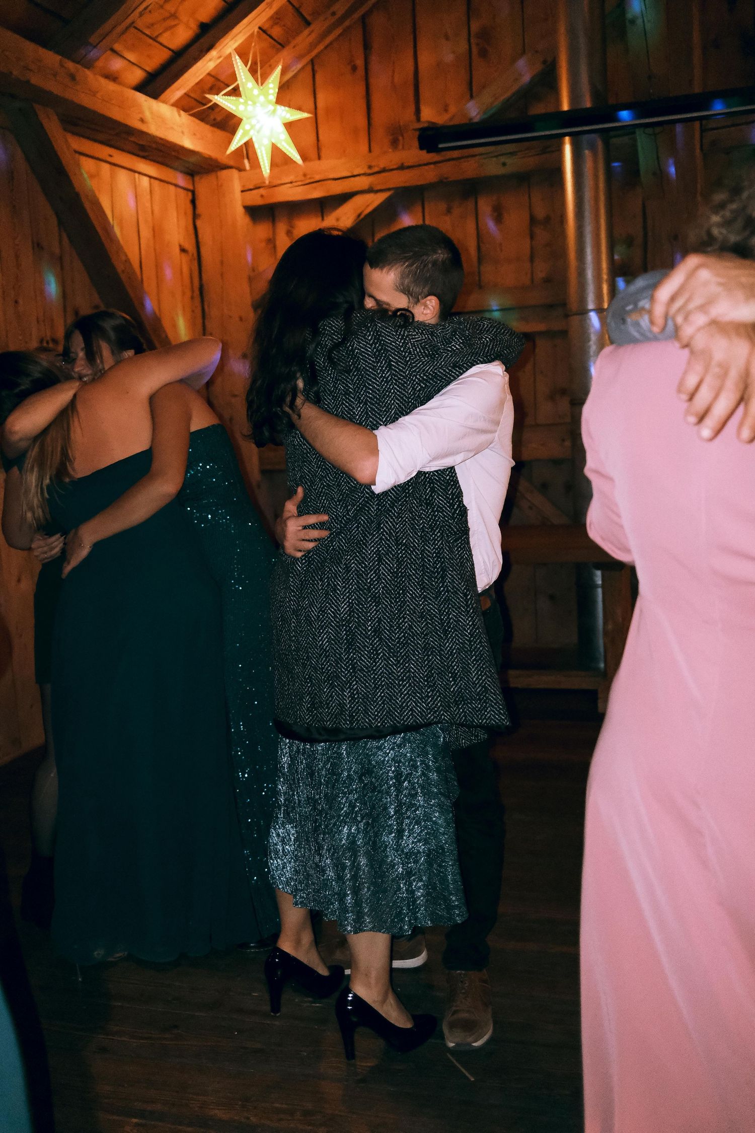 Wedding guests sharing warm embraces on the dance floor in a wooden barn venue.