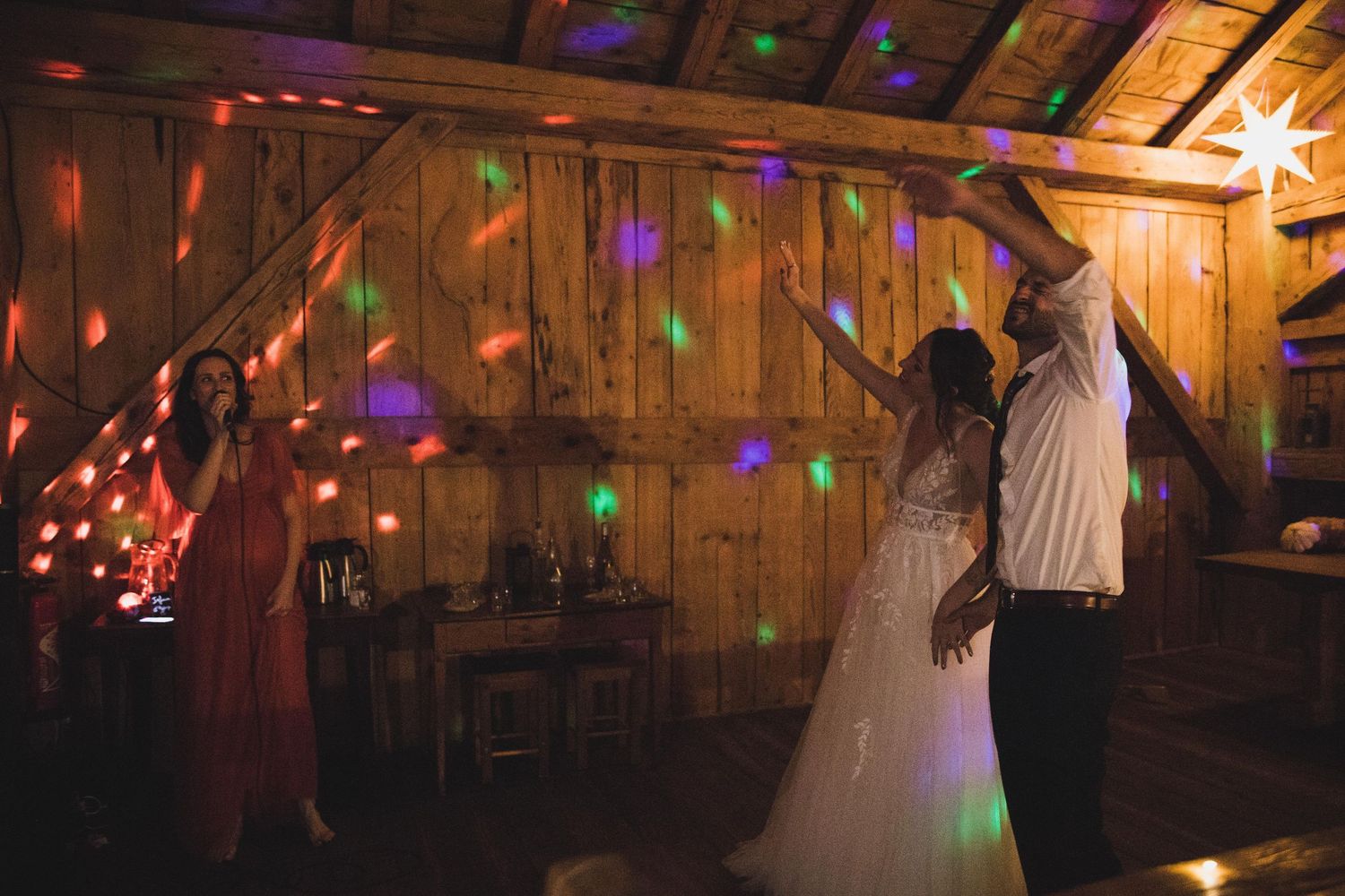 Bride and groom dancing under colorful disco lights in rustic wooden barn venue.