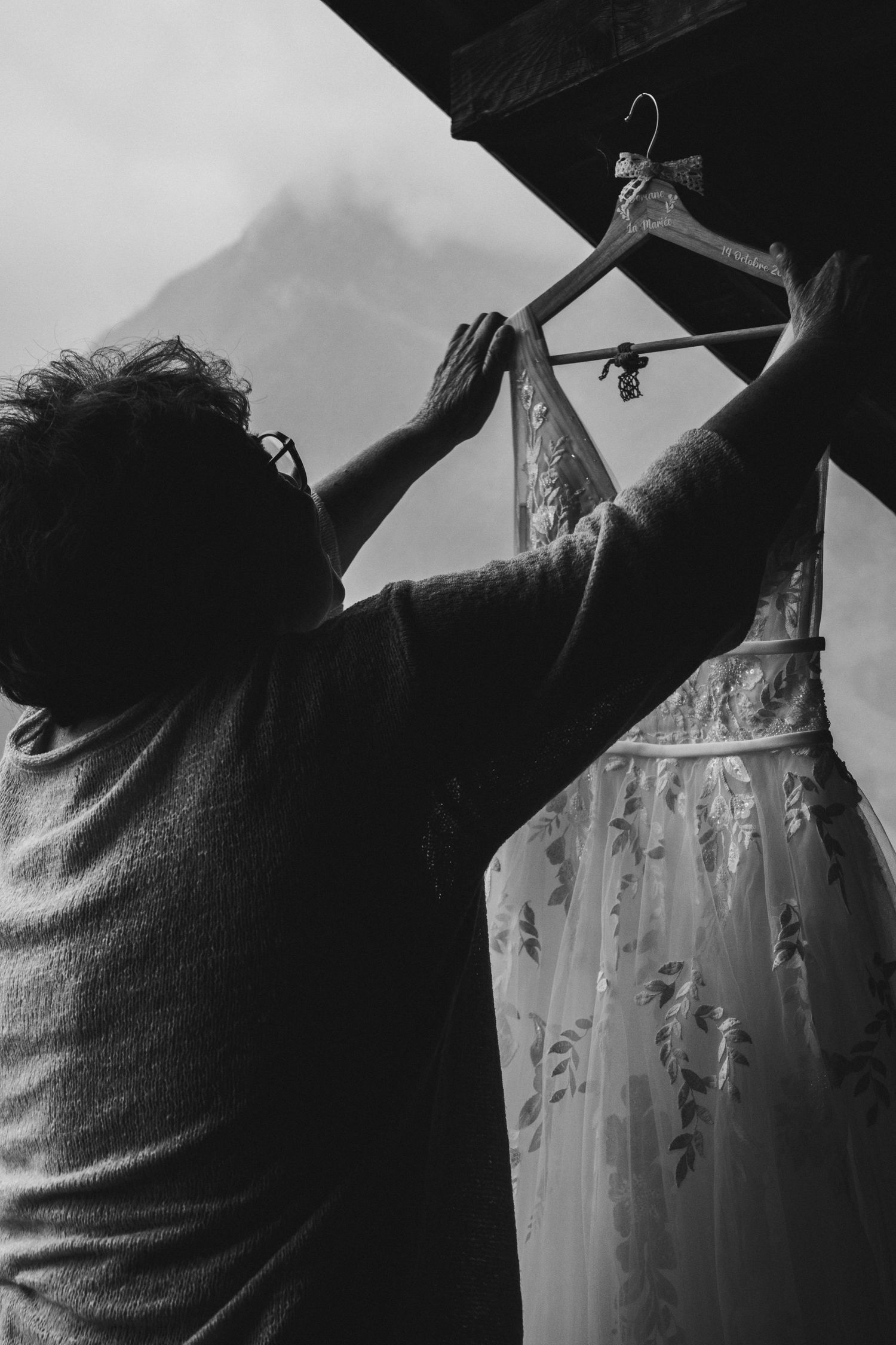 Black and white photo of person hanging wedding dress on hanger with mountain backdrop.