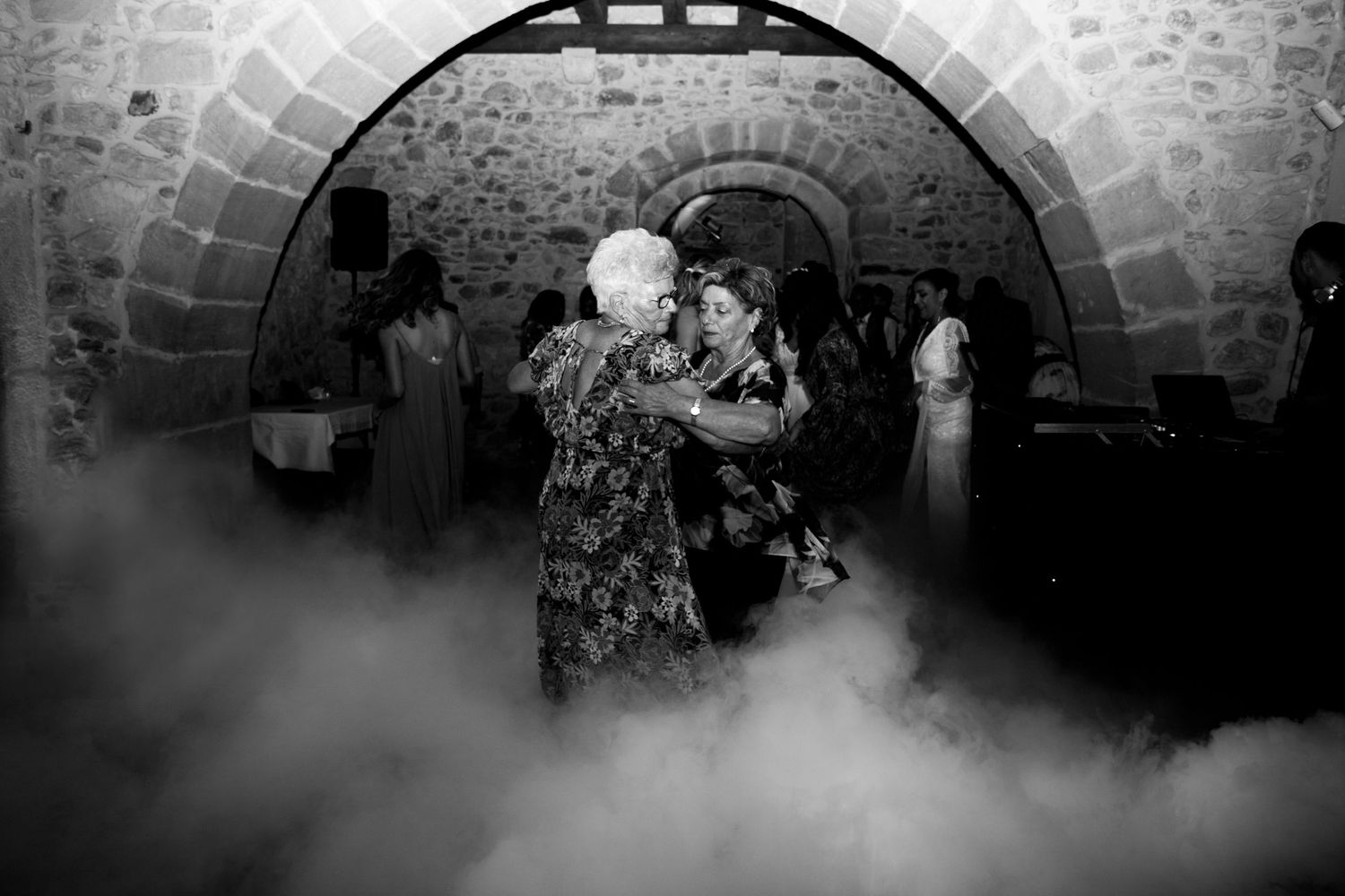 Two women dancing together on foggy dance floor in stone arched wedding venue.