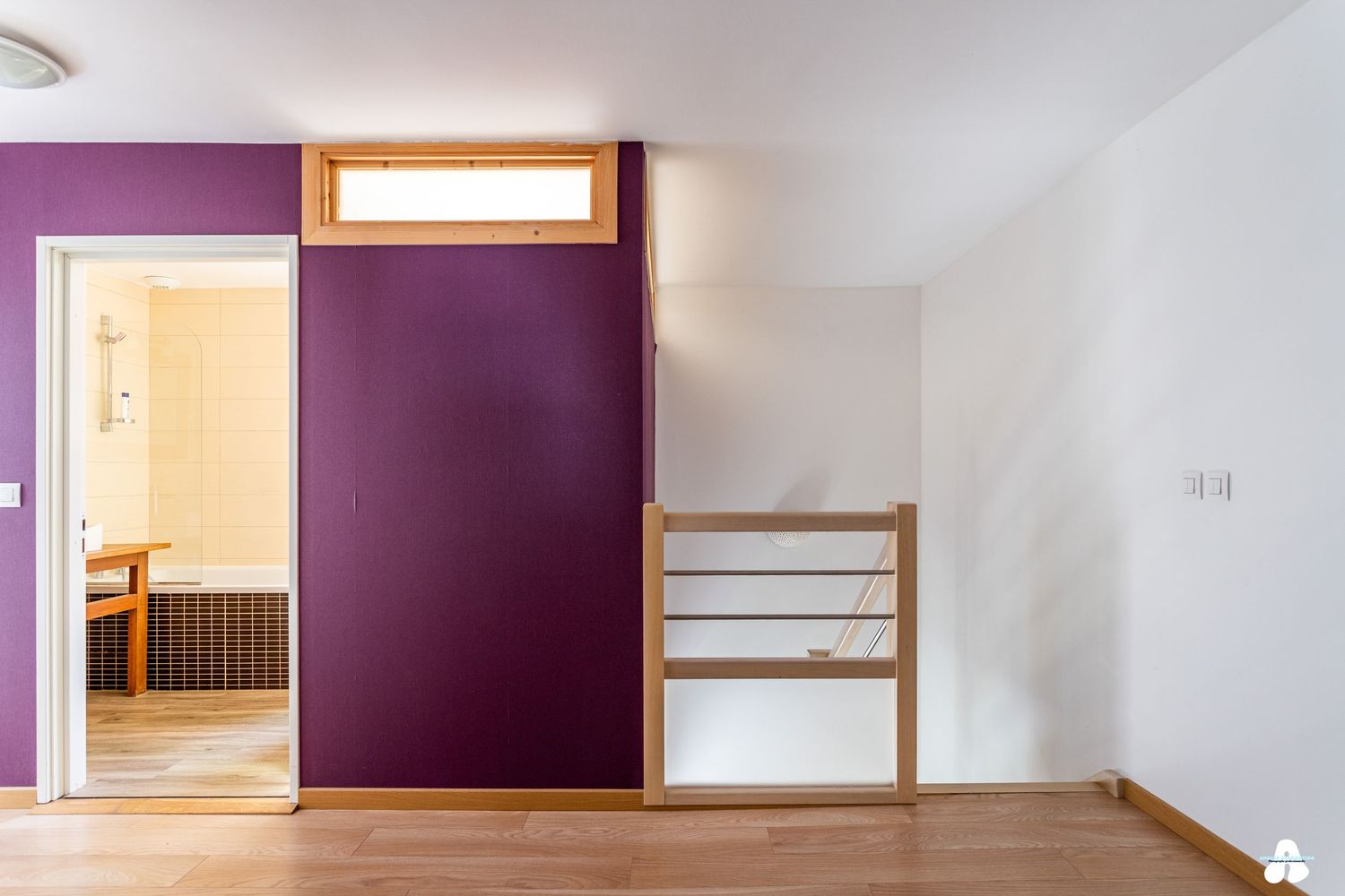 Upper floor landing with purple accent wall, wooden stair railing, and view into bathroom.