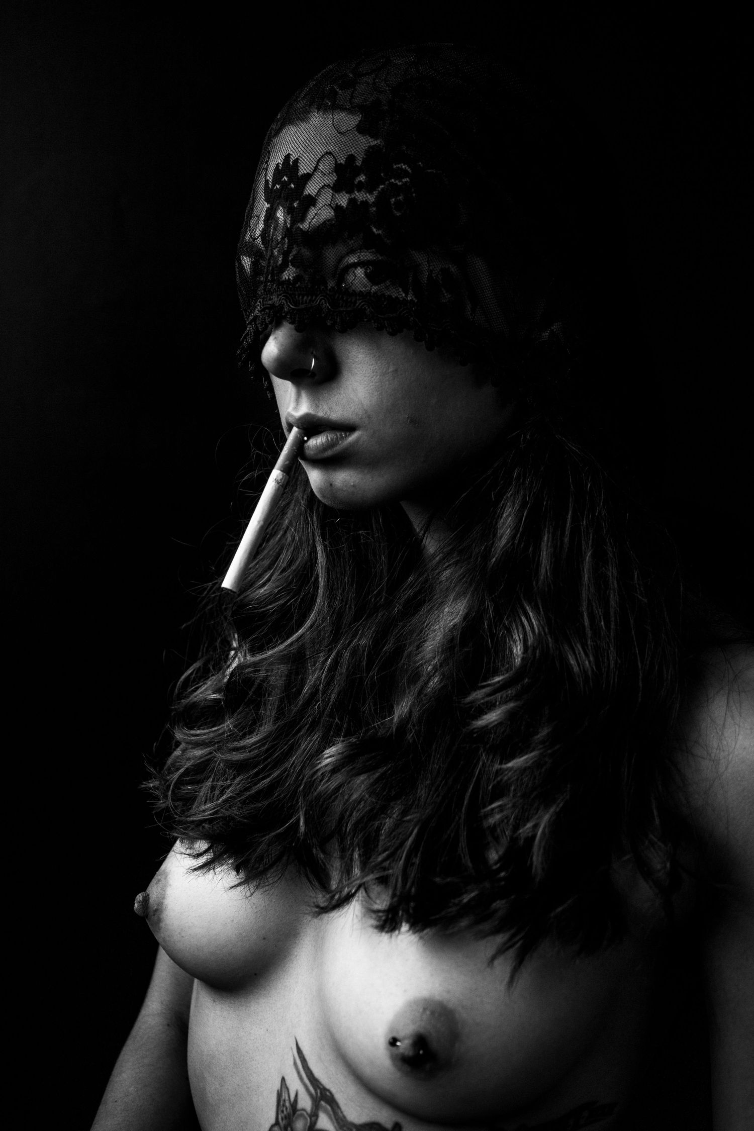 Black and white artistic nude portrait of woman wearing lace mask and smoking cigarette.